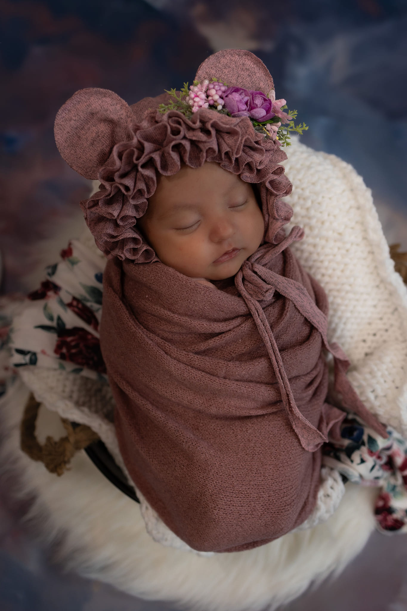 A newborn in a blanket with ear muffs sleeping.