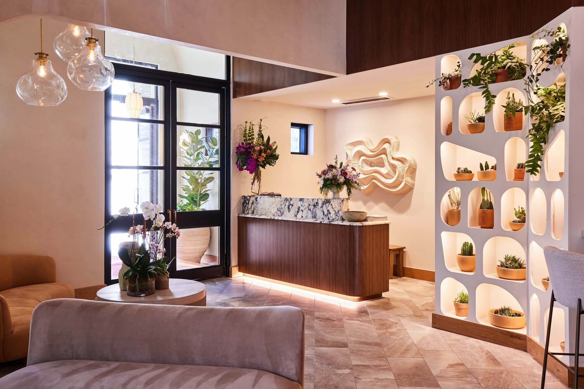 Interior host stand at Delbar Buckhead with marble counter, plush seating, glass pendant lights, and potted plant shelf.
