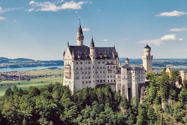 Neuschwanstein castle with a forest in the foreground and a river behind it