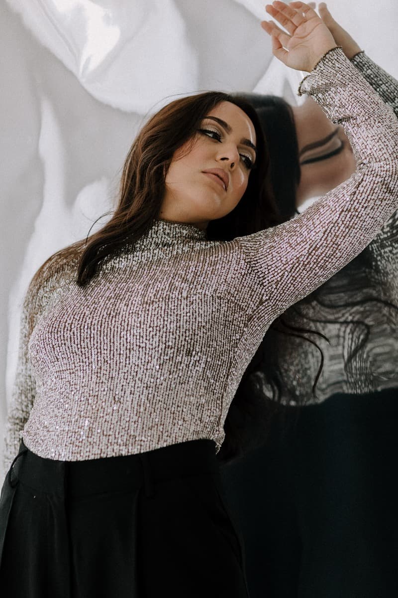 A model poses with her arm raised against a reflective background in a silver top, emphasizing movement and texture during a Mylar shoot at Revelator Studio, Shreveport.