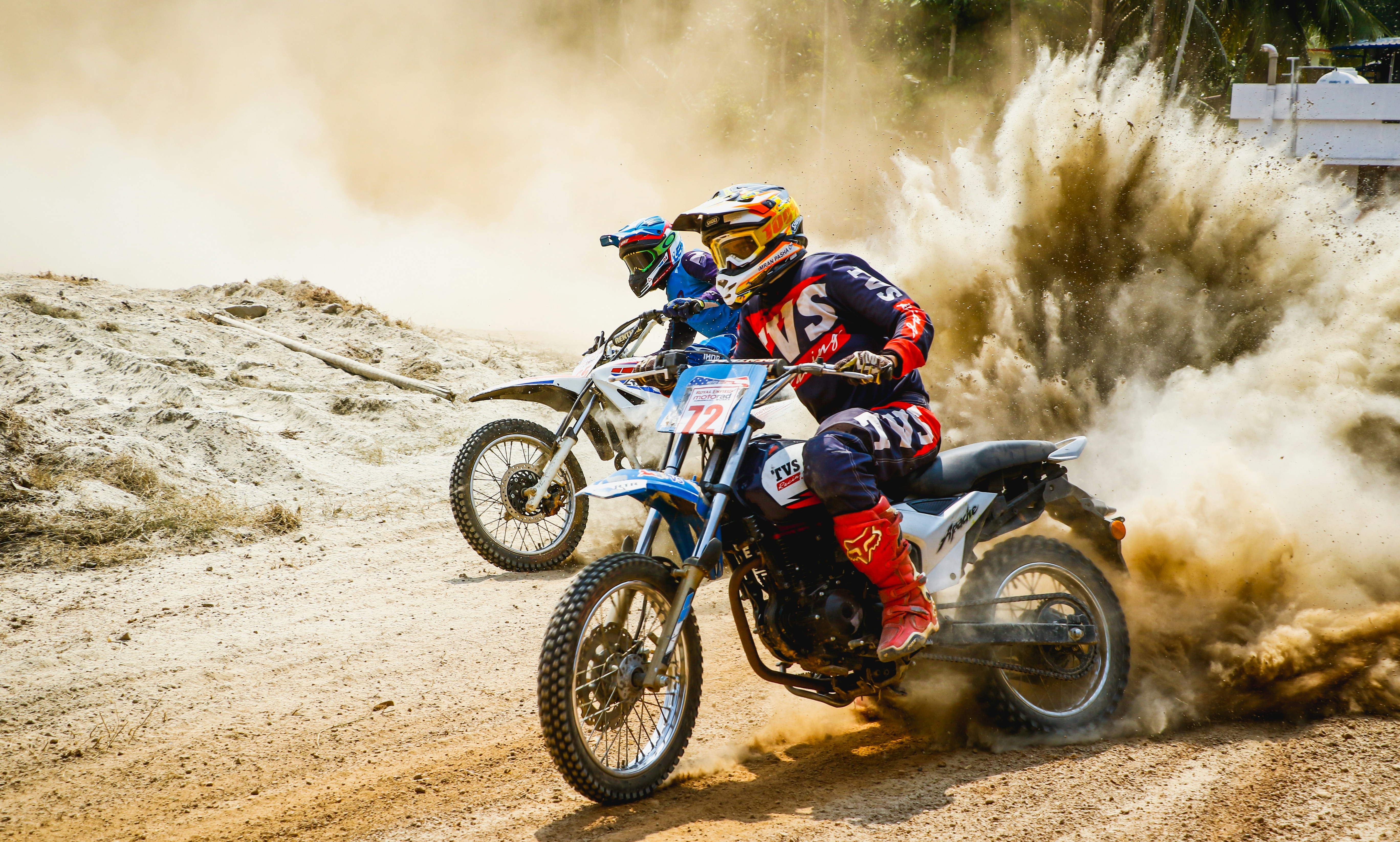 two men riding motocross bikes on brown sand