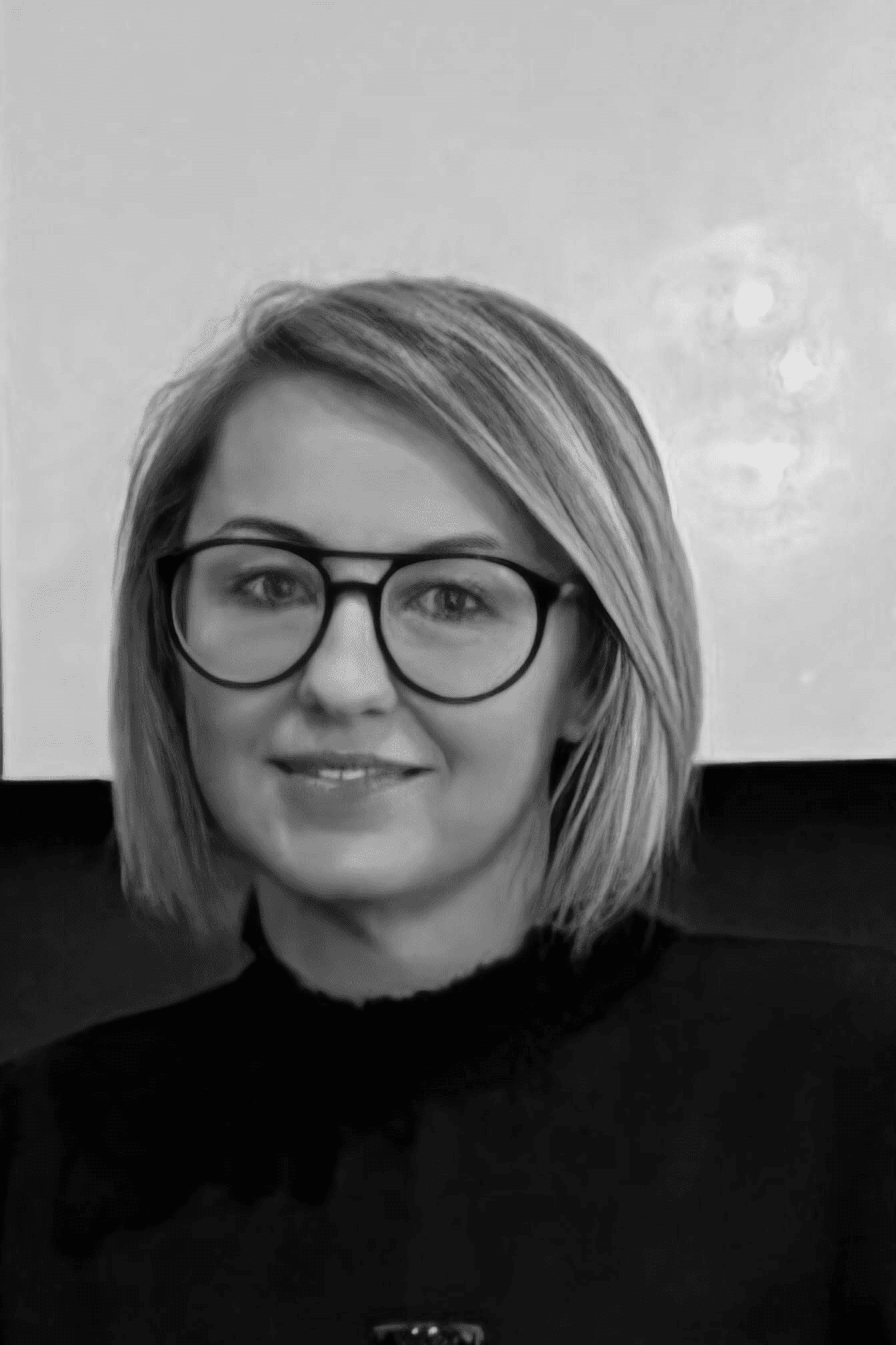 Porträt einer jungen Frau mit Brille, die lächelt. Sie hat kurze blonde Haare und trägt einen schwarzen Pullover.