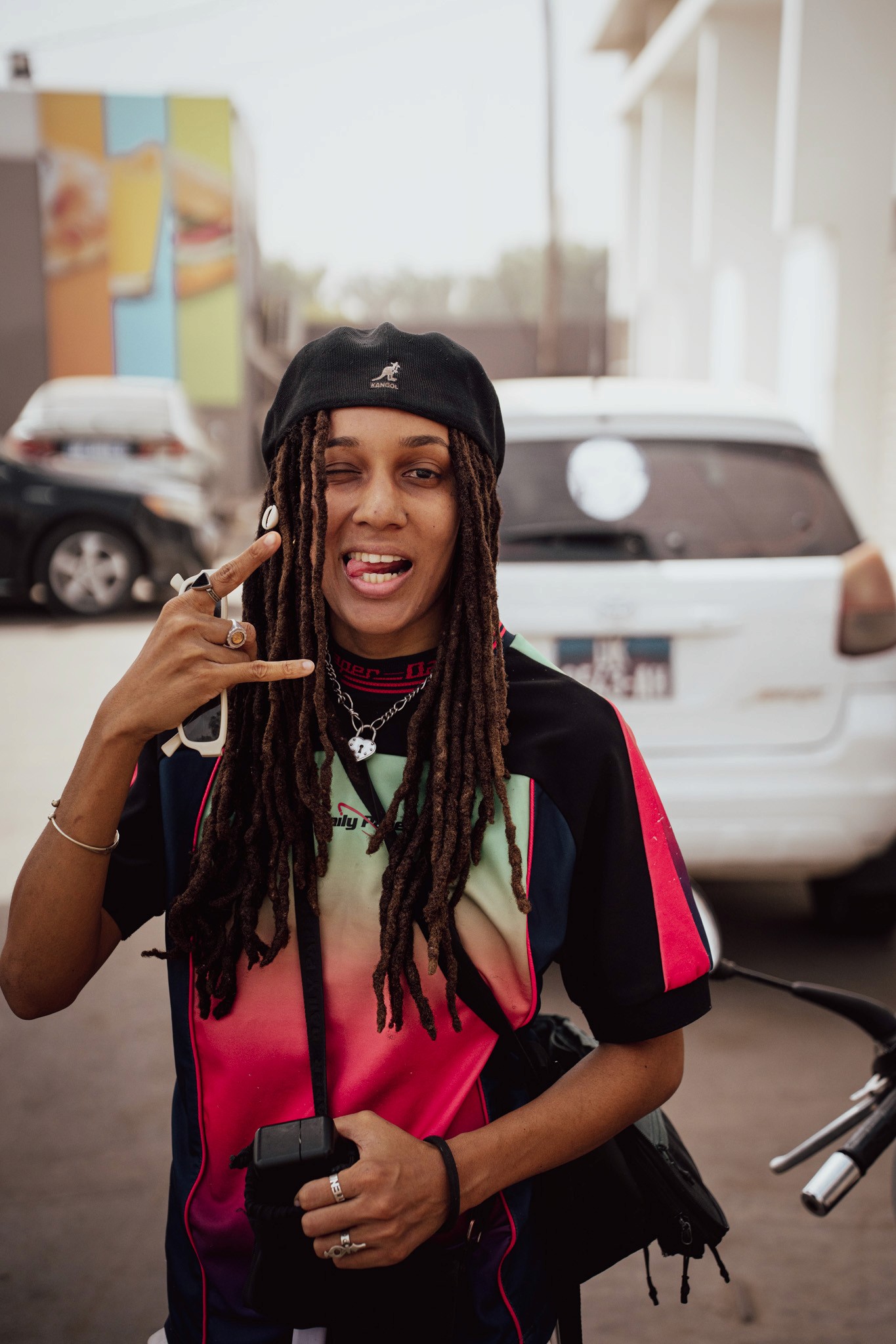 A woman in a white blouse and dark vest sits on a park bench, looking away and smiling. A ukulele rests next to her.