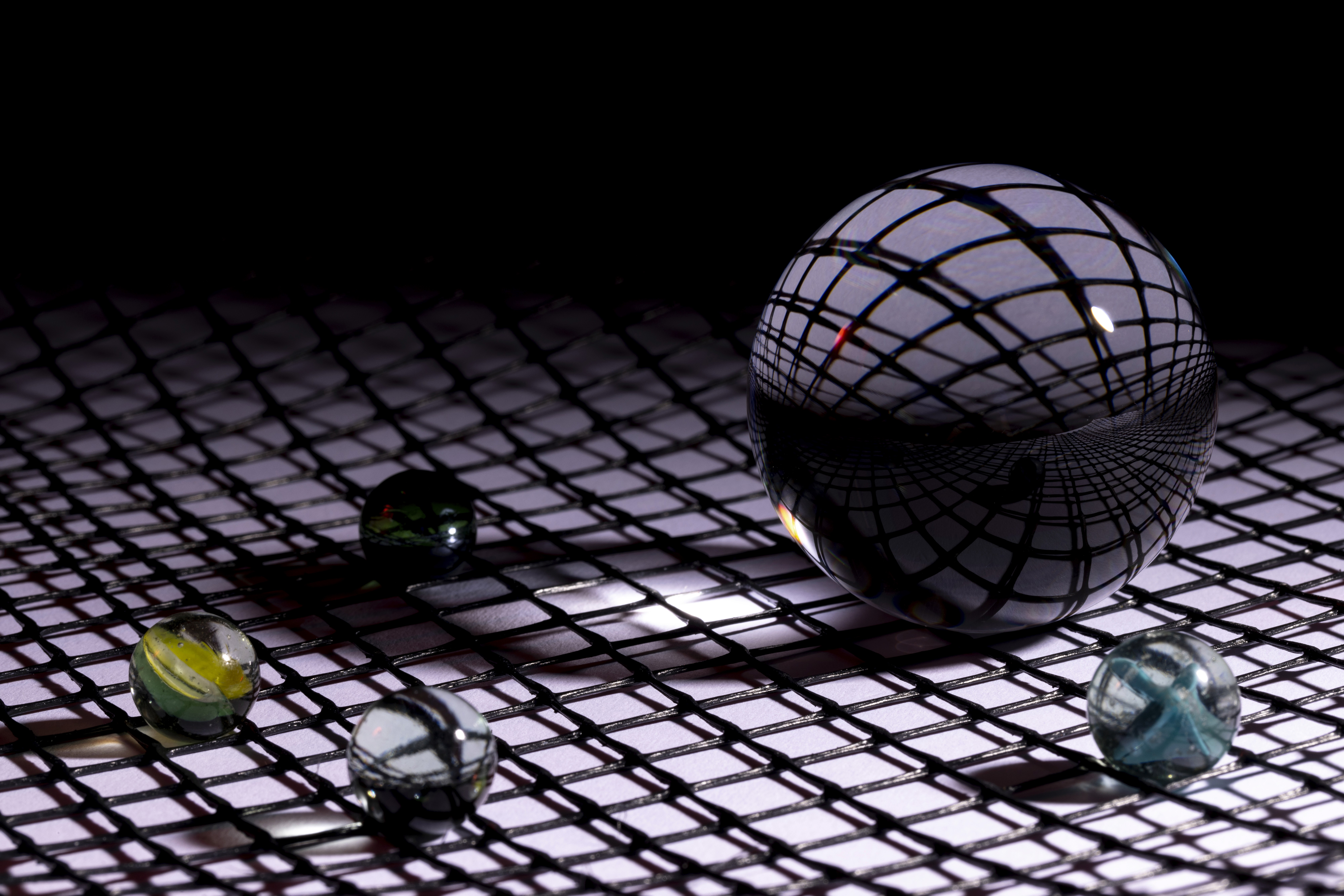 Two coworkers having a discussion at a round desk in a modern office, with laptops, papers, and a large glass wall in the background.