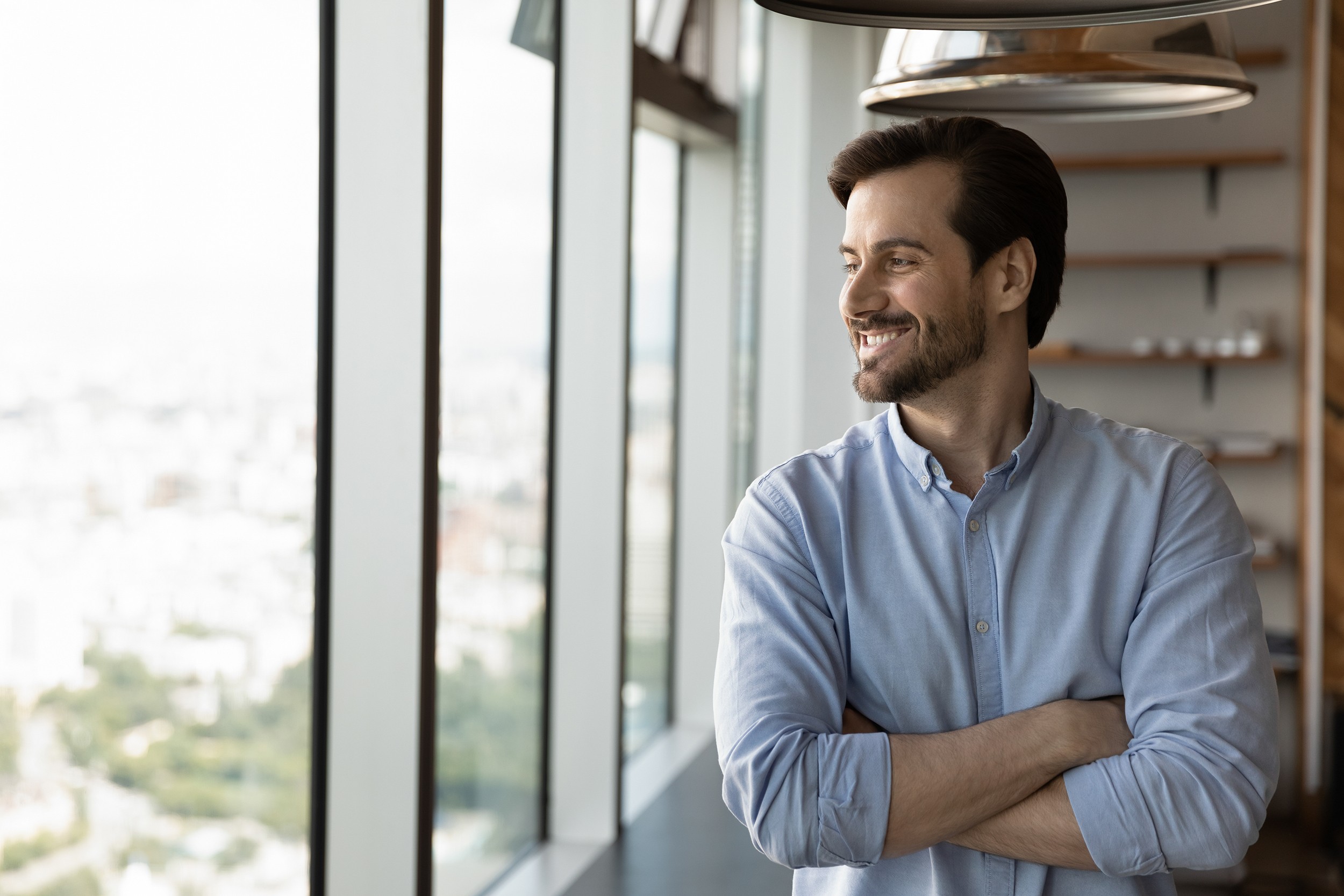 Happy young Caucasian businessman look in window distance planning or thinking of perspectives and opportunities. Smiling male employee dream or visualize career success. Business vision concept.