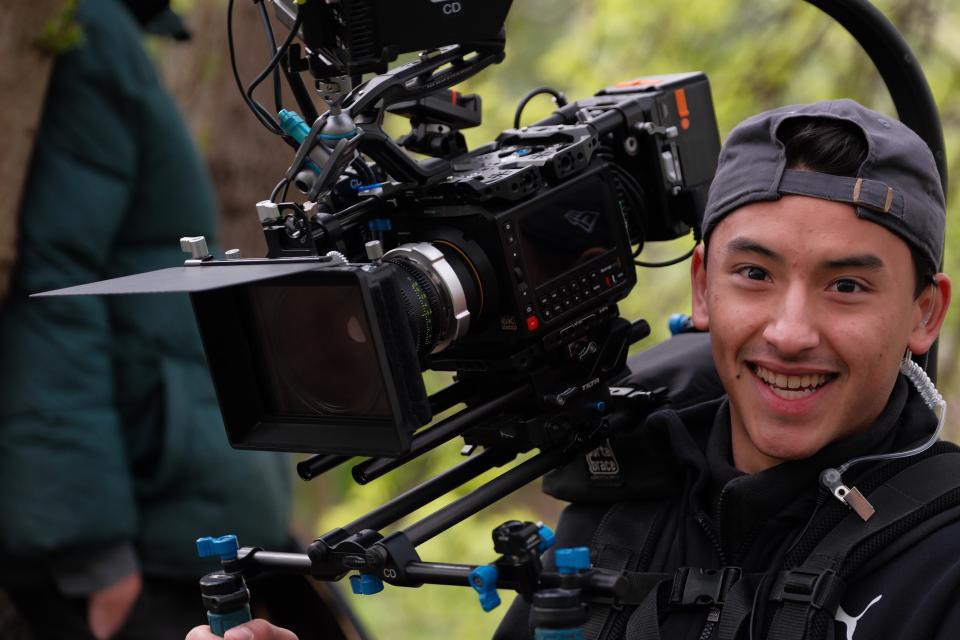 A person with wavy, shoulder-length hair wears a cream beanie and a matching thick-knit sweater over a gray shirt, giving a cozy, relaxed vibe.