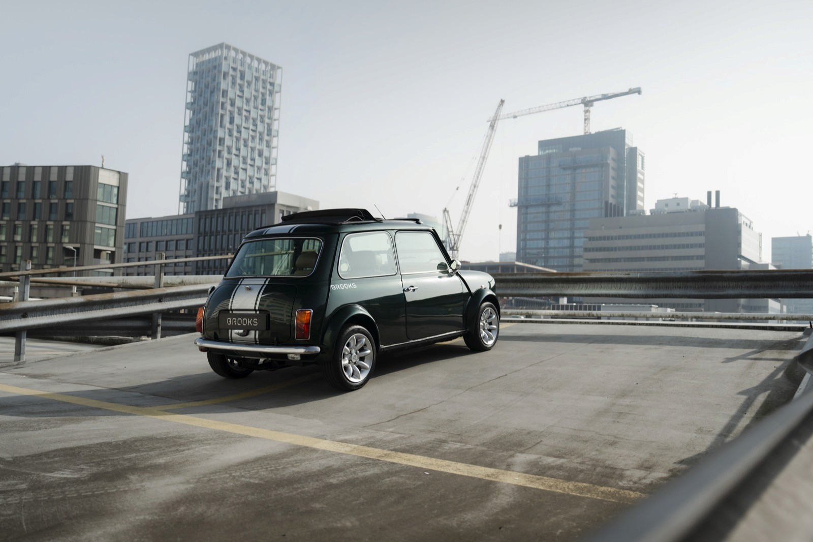 A taxi parked on a roadway with modern buildings and construction cranes in the background under a hazy sky.