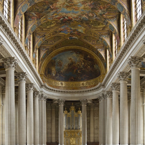 Ornate hall with tall columns, a grand ceiling adorned with elaborate frescoes, and a large gold-framed organ at the far end.