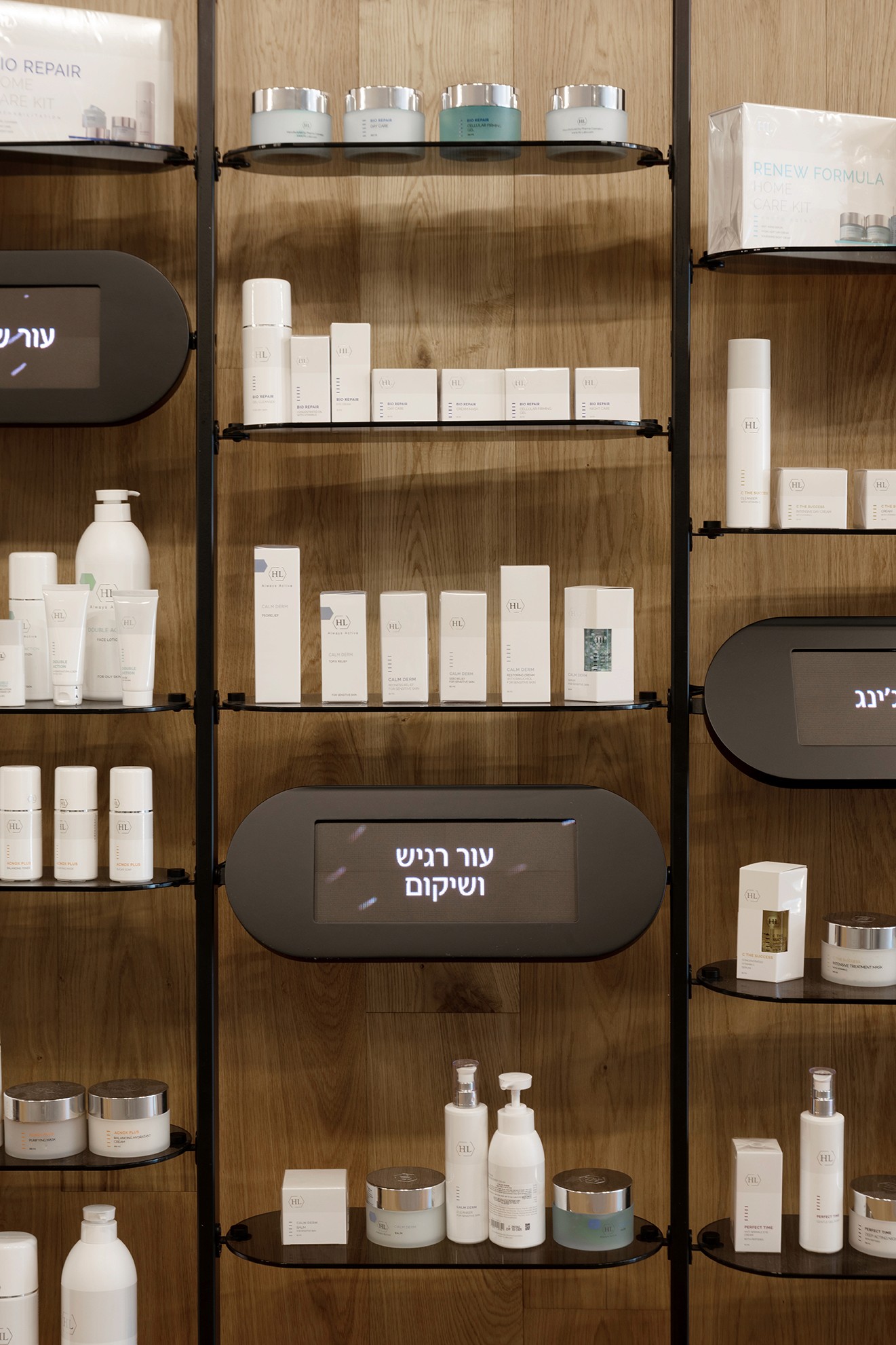 עיצוב קמעונאי (Retail Design): קיר תצוגה באורך מלא המשלב מדפי זכוכית מרחפים על גבי עמודי מתכת, על רקע חיפוי עץ חמים.