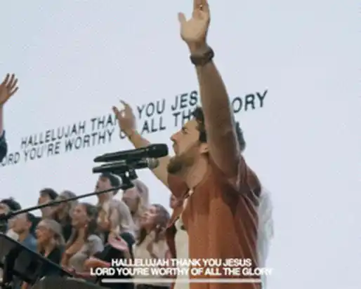 Worship leader with hands raised as lyrics fill the screen behind him