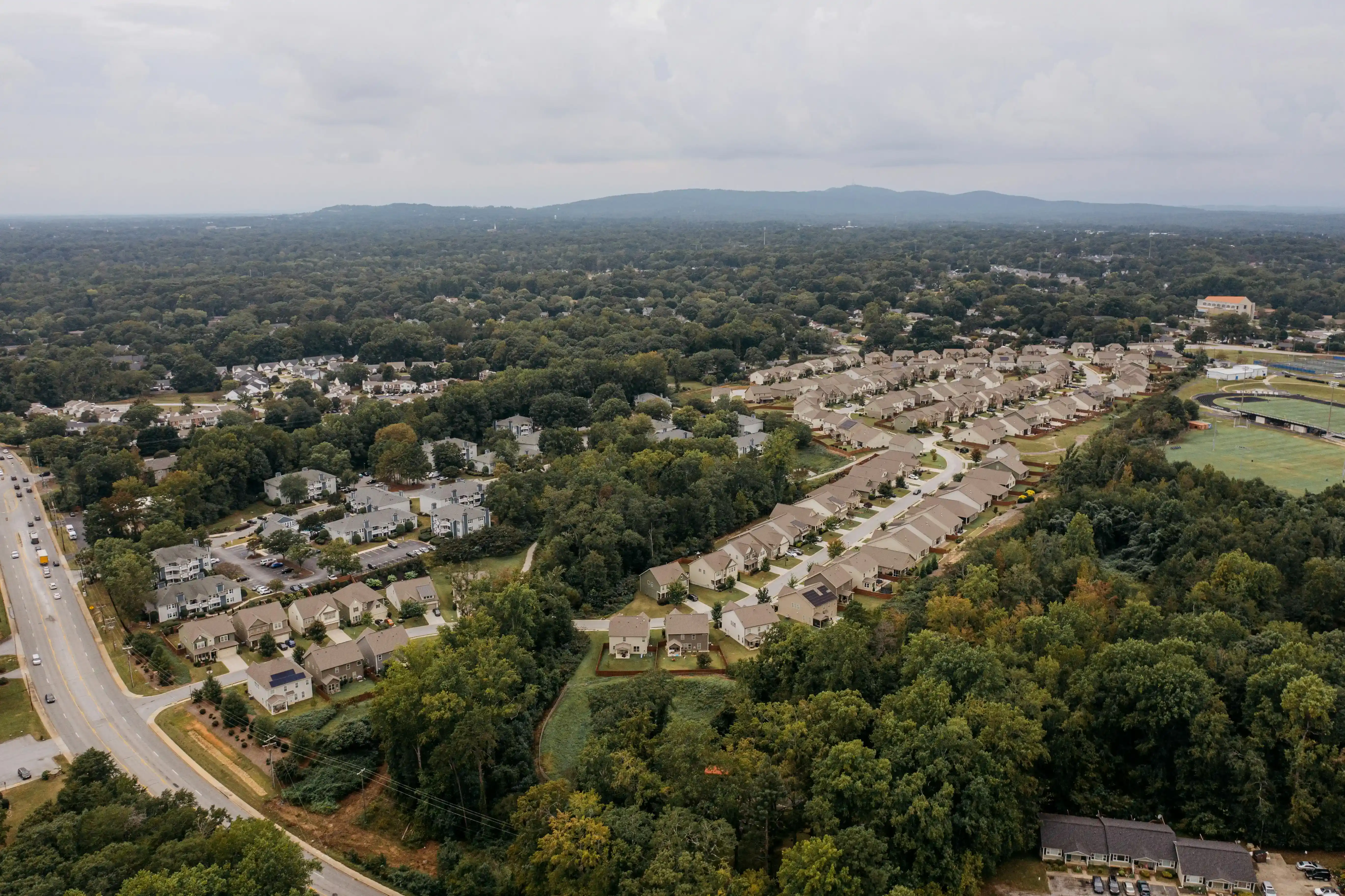 Aerial view of a suburban neighborhood with houses, roads, and surrounding trees