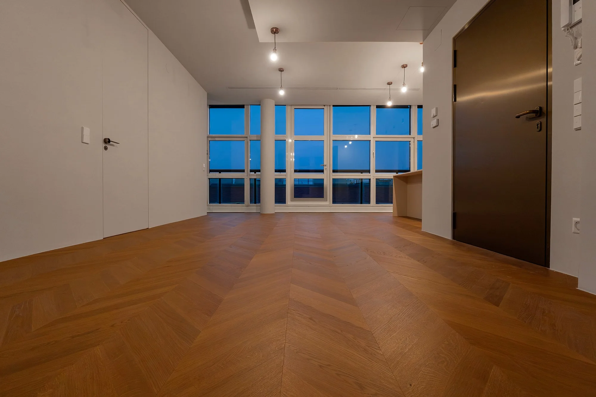 Wohnraum in Abendstimmung mit großer Fensterfront und frisch verlegtem Chevron-Parkettboden.