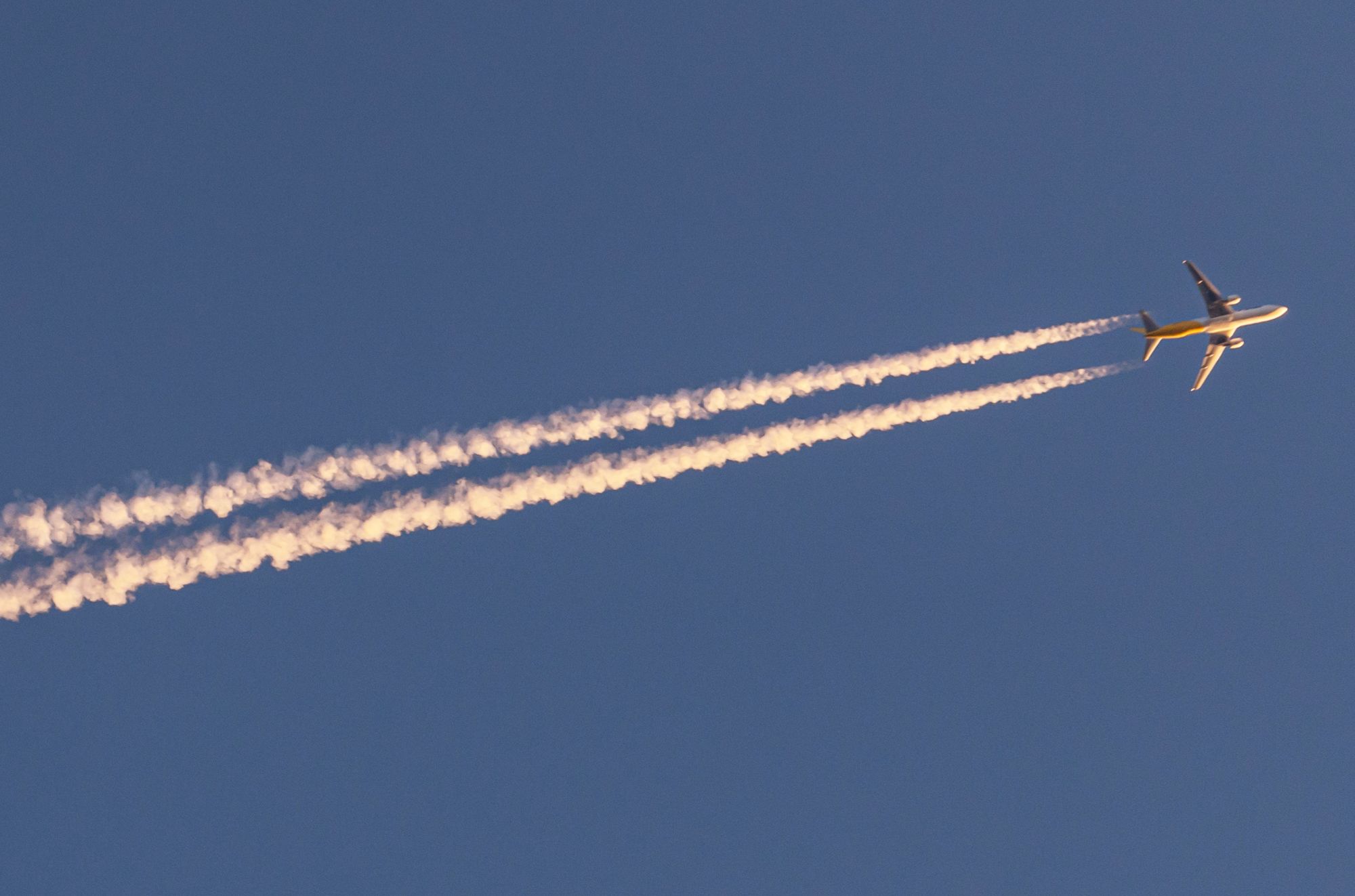 Commercial aircraft leaving two long persistent chemtrails across a clear blue sky