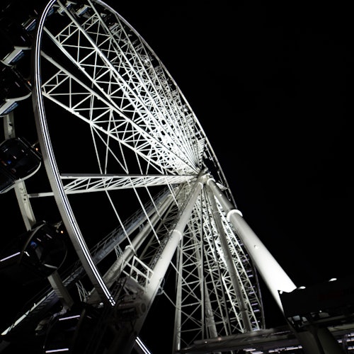 Rueda de la fortuna iluminada vista desde abajo por la noche, con un cielo oscuro de fondo y la estructura metálica visible.