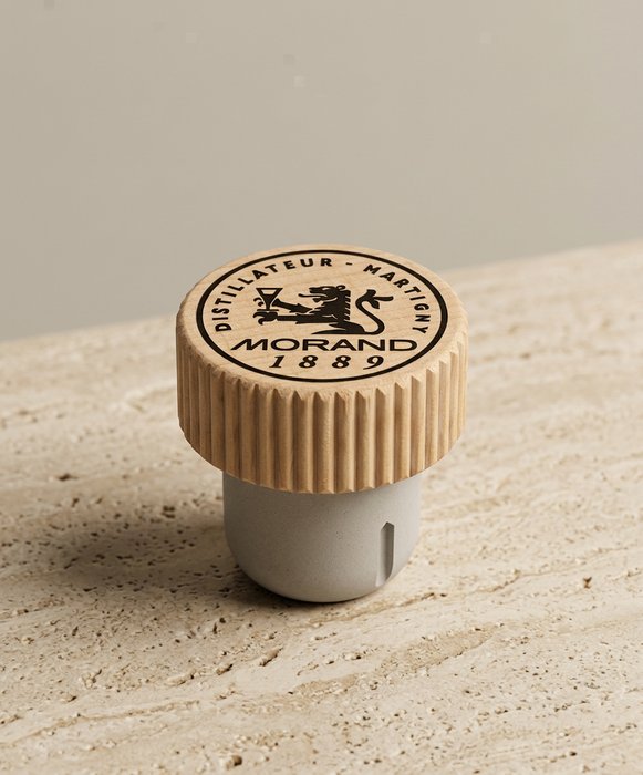 Wooden bottle stopper with a black logo on a beige surface.