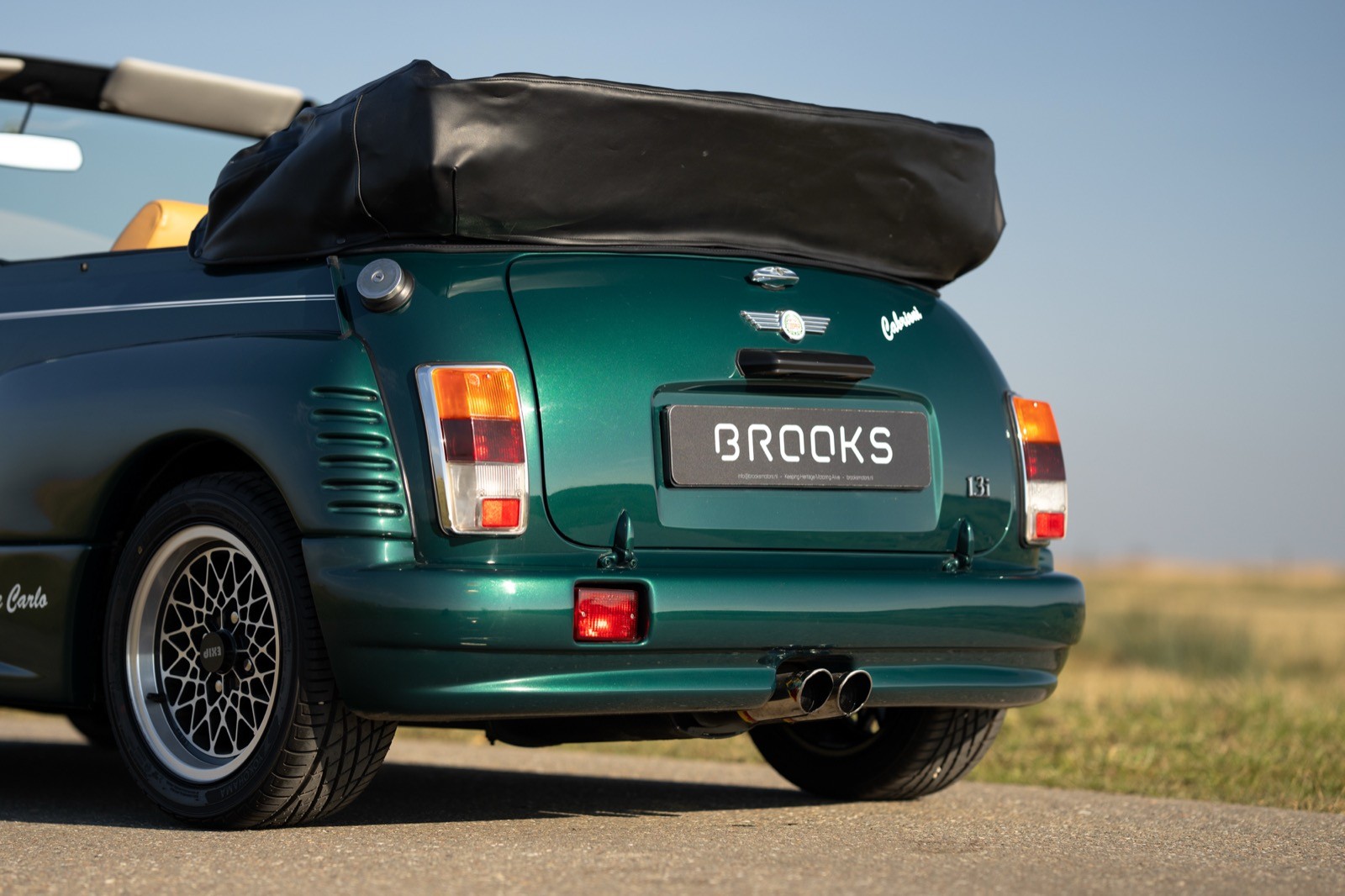 A green convertible car parked in an open area with the roof down, showcasing its rear view against a clear sky.