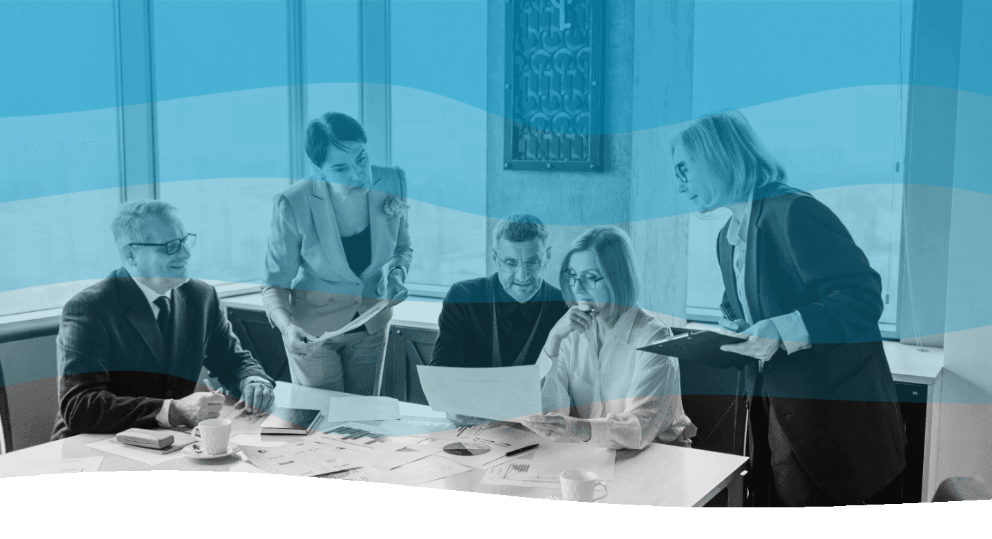 A diverse group of professionals engages in a collaborative meeting around a conference table, reviewing documents and discussing strategies in a modern office setting.