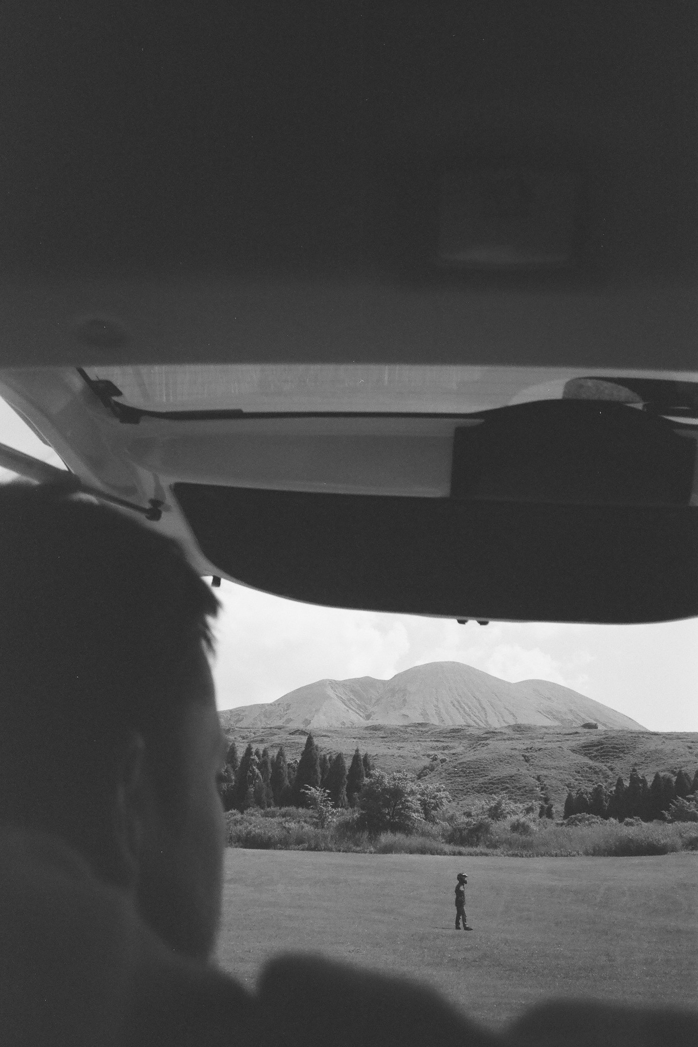 Analog photo of a man viewing a field and mountain with a bike rider in the distance.