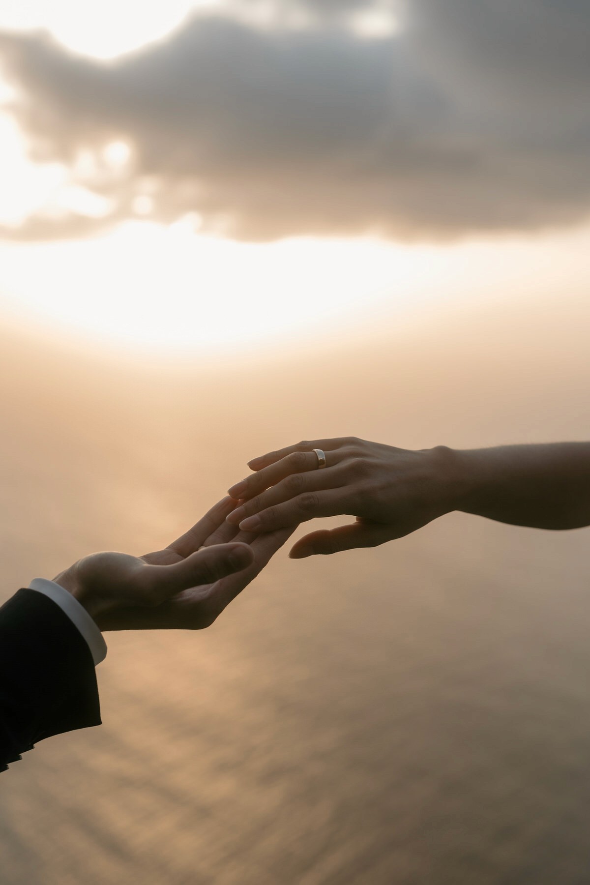 hands with wedding bands over atlantic ocean sunset