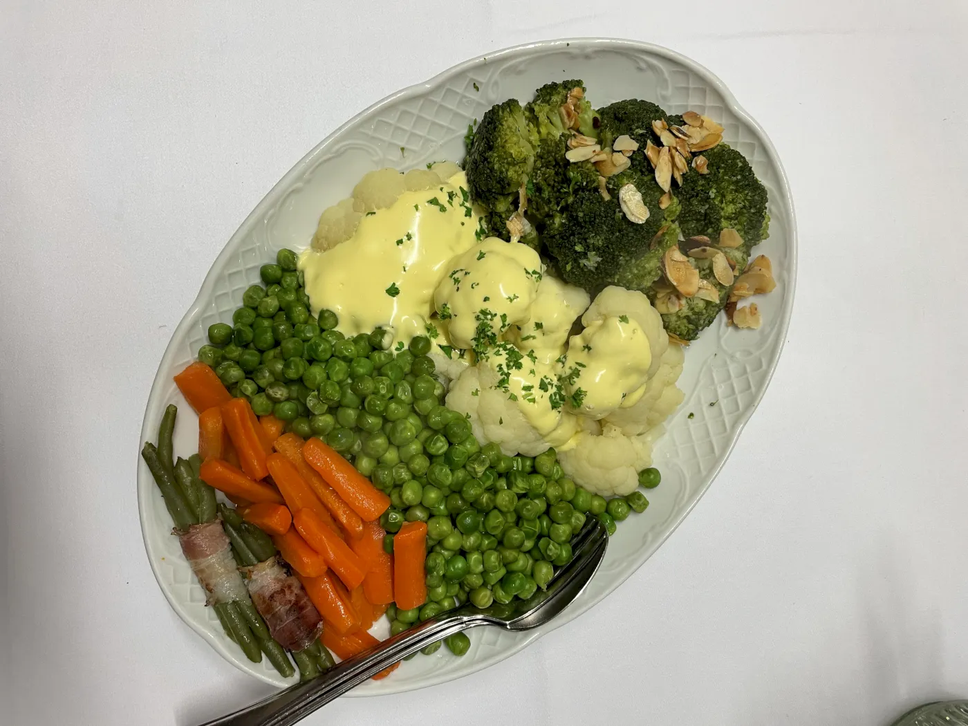 Erbsen, Möhren, Blumenkohl, Brokoli, mit Hollandaise Soße, serviert auf einem Teller.