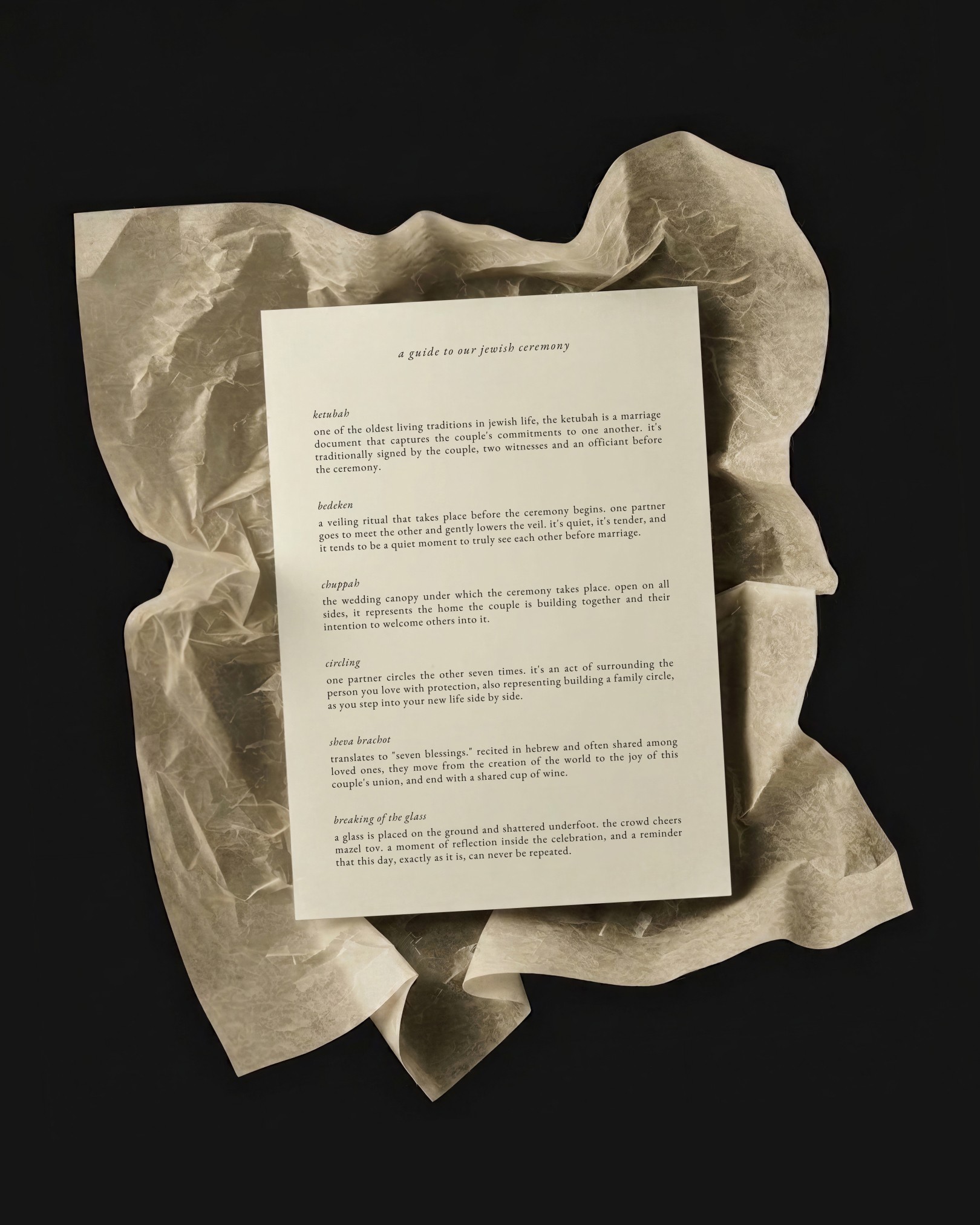 Printed Jewish wedding ceremony guide resting on crumpled tissue paper on a dark background