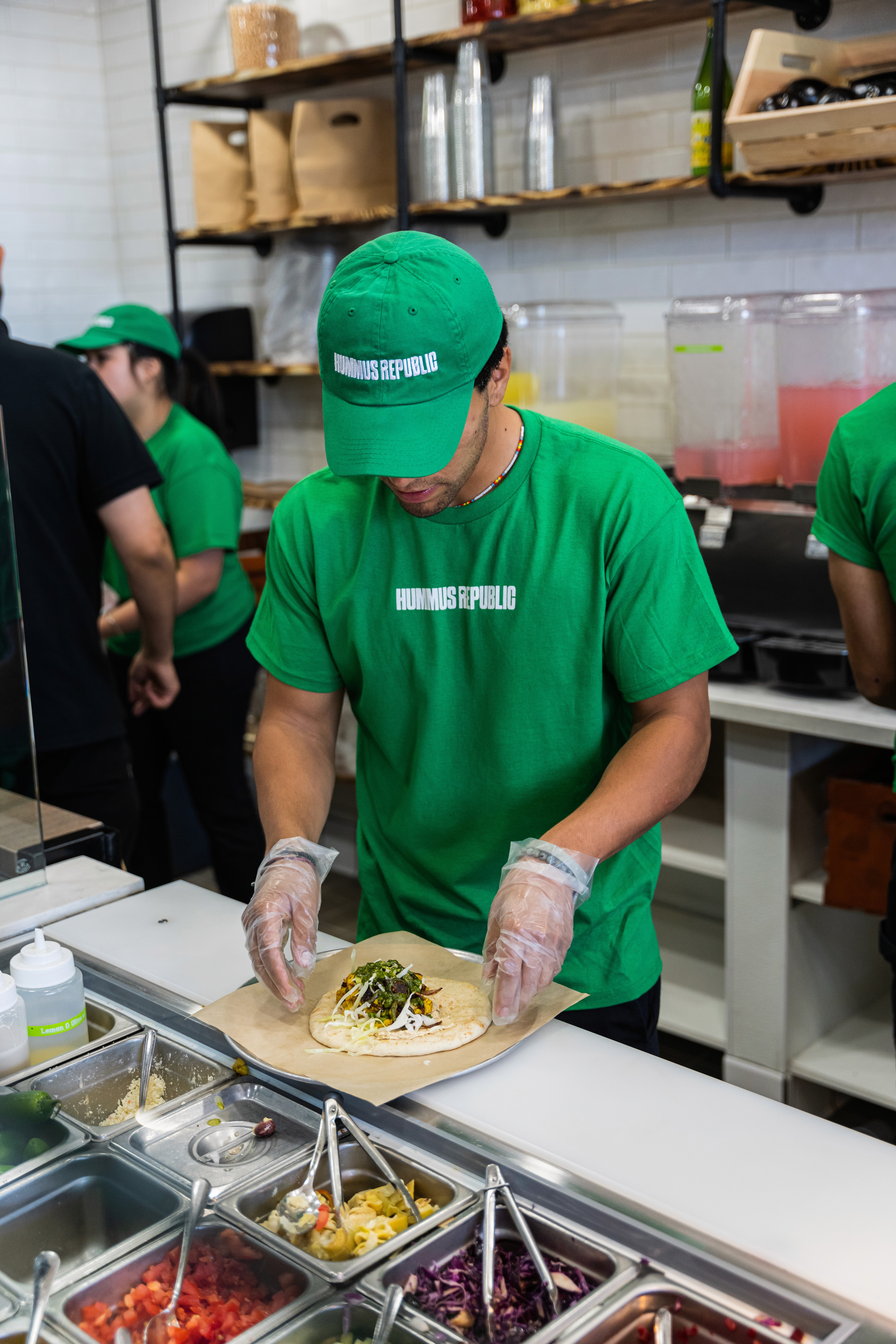 employee assembeling a pita with a green hat and green shirt on