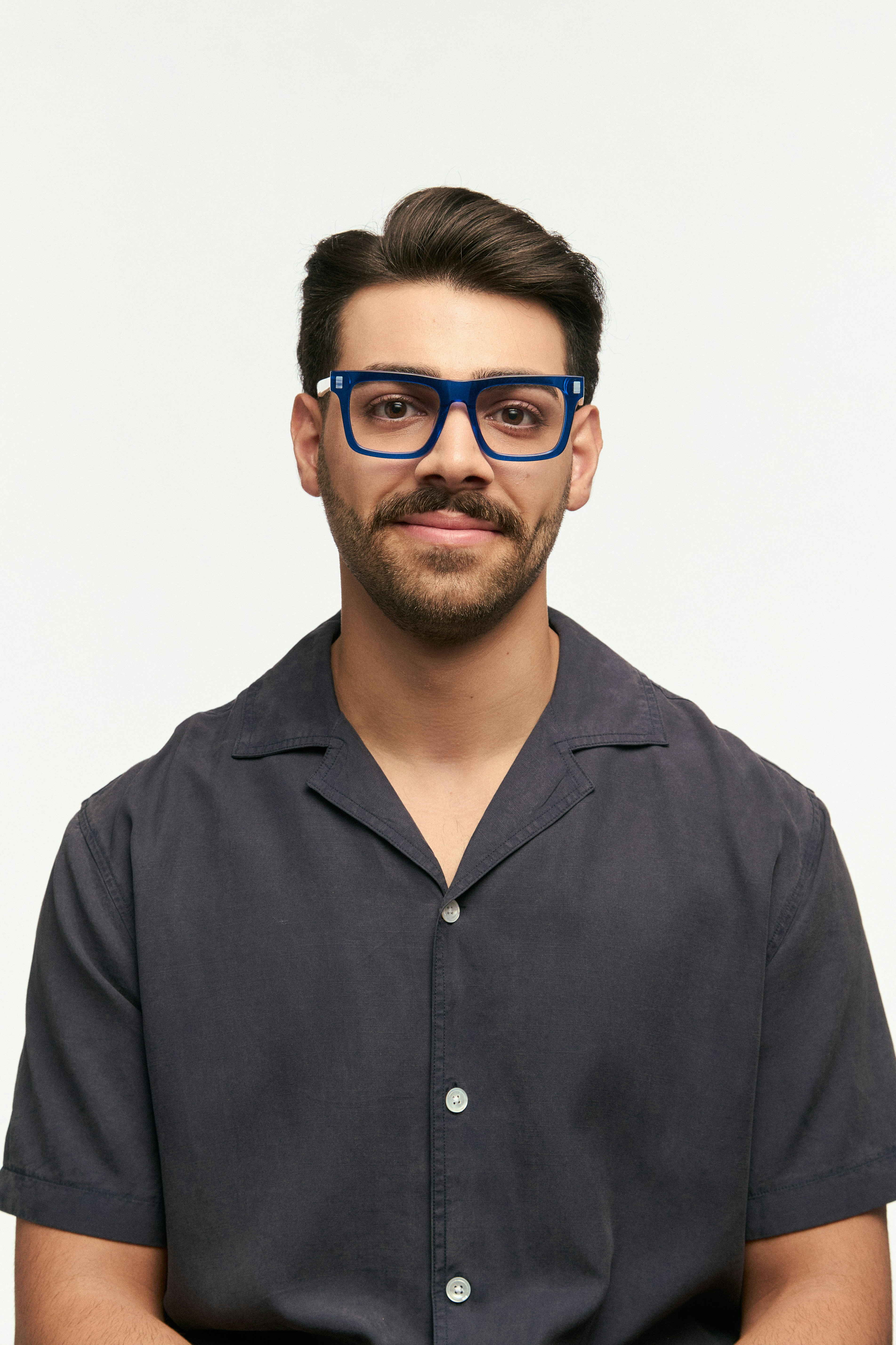 A man with blue glasses smiles at the camera.