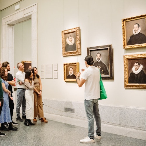 מדריך במוזיאון מציג לקבוצה של חמישה אנשים סדרה של דיוקנאות ממוסגרים על הקיר.