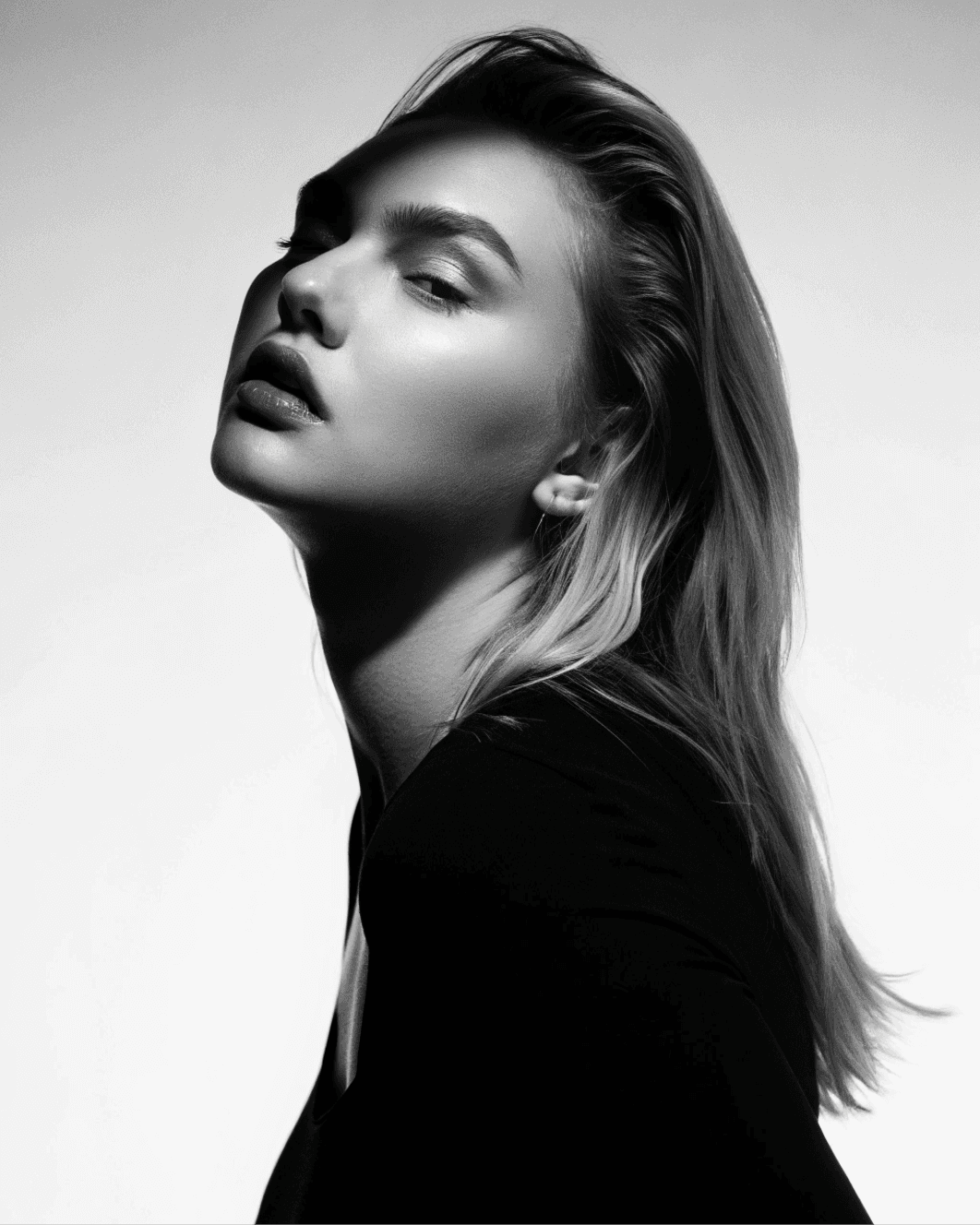 A black-and-white portrait of a model with her head tilted and eyes closed, showcasing natural beauty and serene expression.