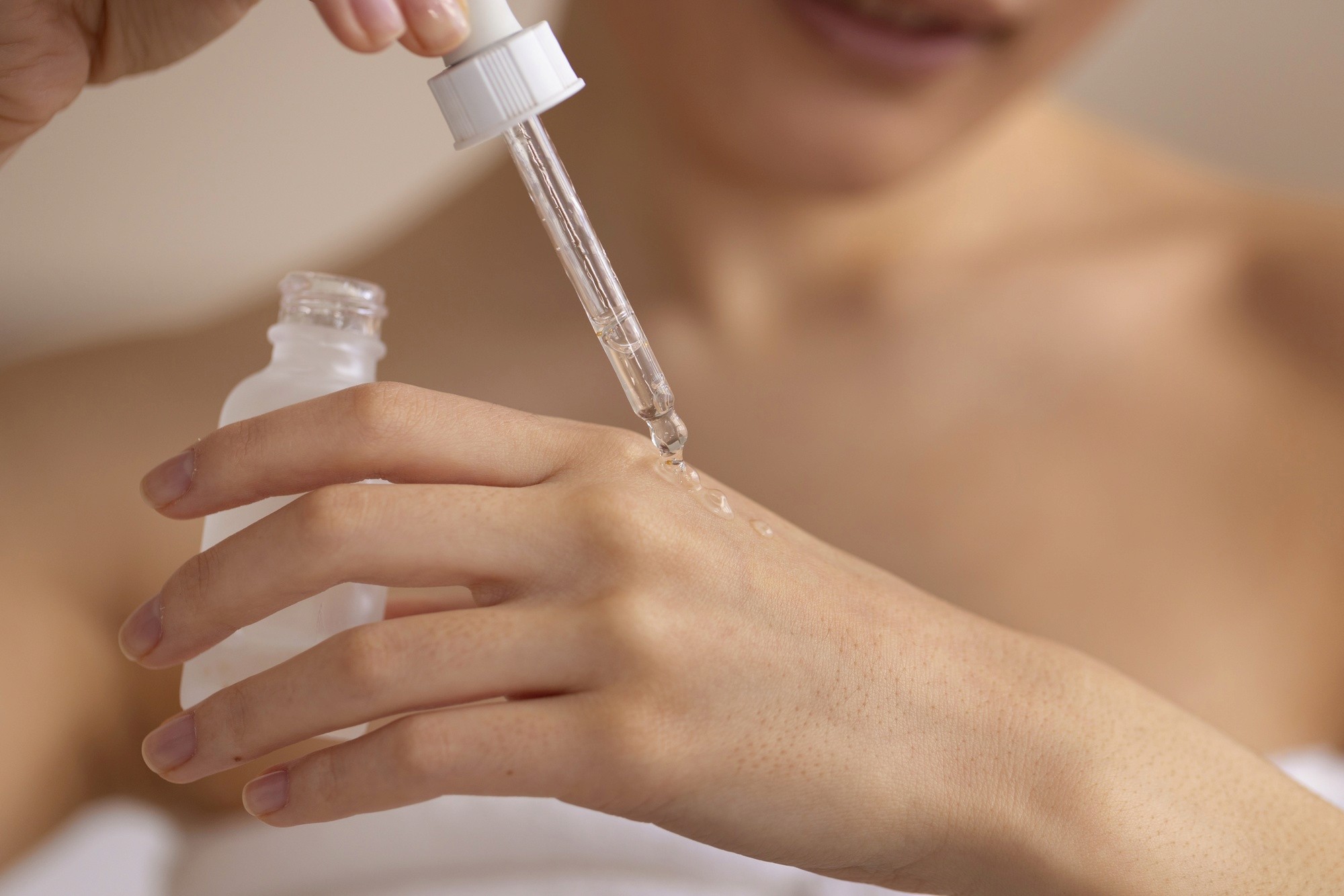 Close-up of a woman applying serum drops onto her hand using a dropper bottle