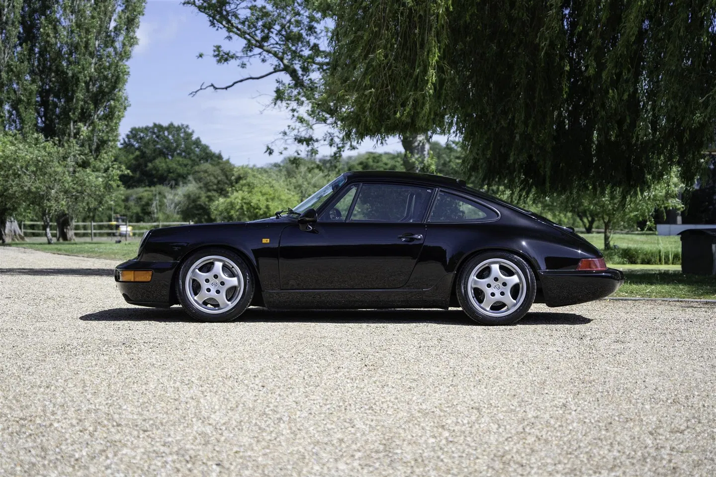 Side profile of the black Porsche 964 RS Lightweight on a gravel driveway