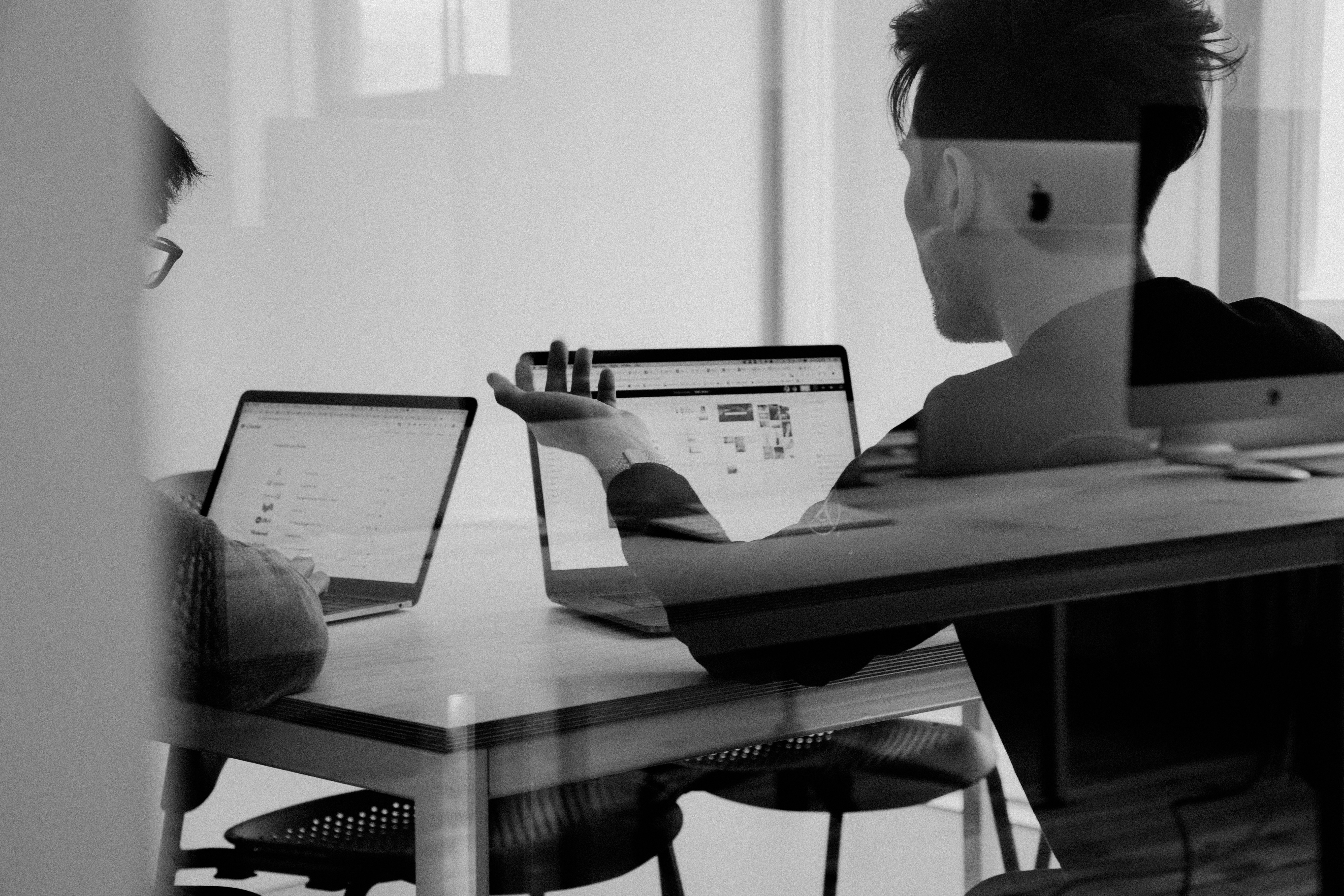 Two people having a discussion while using their laptops.