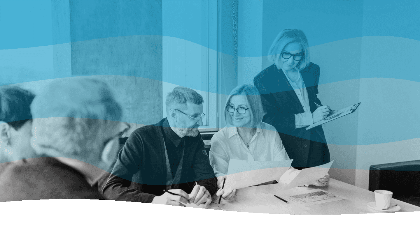 A group of diverse women in a professional meeting setting, with one woman standing confidently in front of a presentation board while two others sit and engage attentively, showcasing teamwork and collaboration.