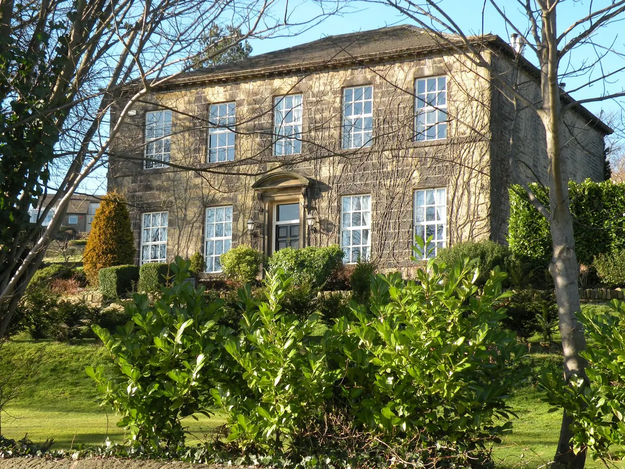 Stone manor house with clean sandstone walls behind a leafy garden