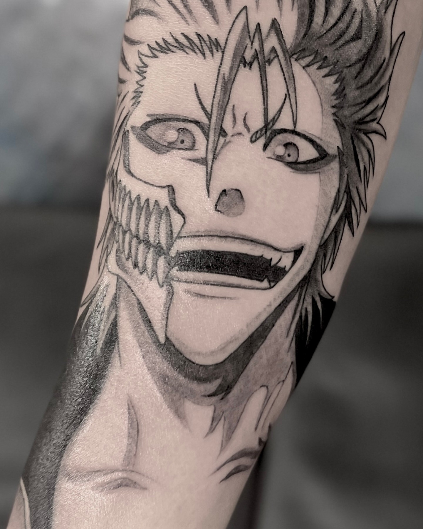 A vibrant tattoo of a chainsaw-like creature on a person's forearm. The tattoo is detailed with shades of orange, black, teal, and red.
