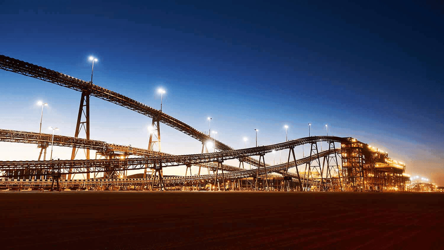 Elevated conveyor belts and floodlit loading structures at a bulk handling terminal at dusk