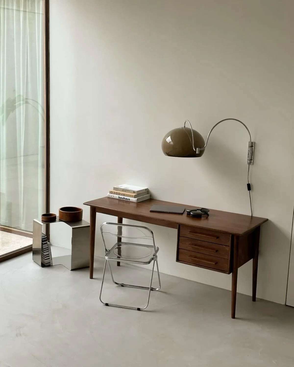 Un espacio de trabajo moderno con un escritorio de madera, una lámpara elegante y una decoración minimalista sobre una pared clara.