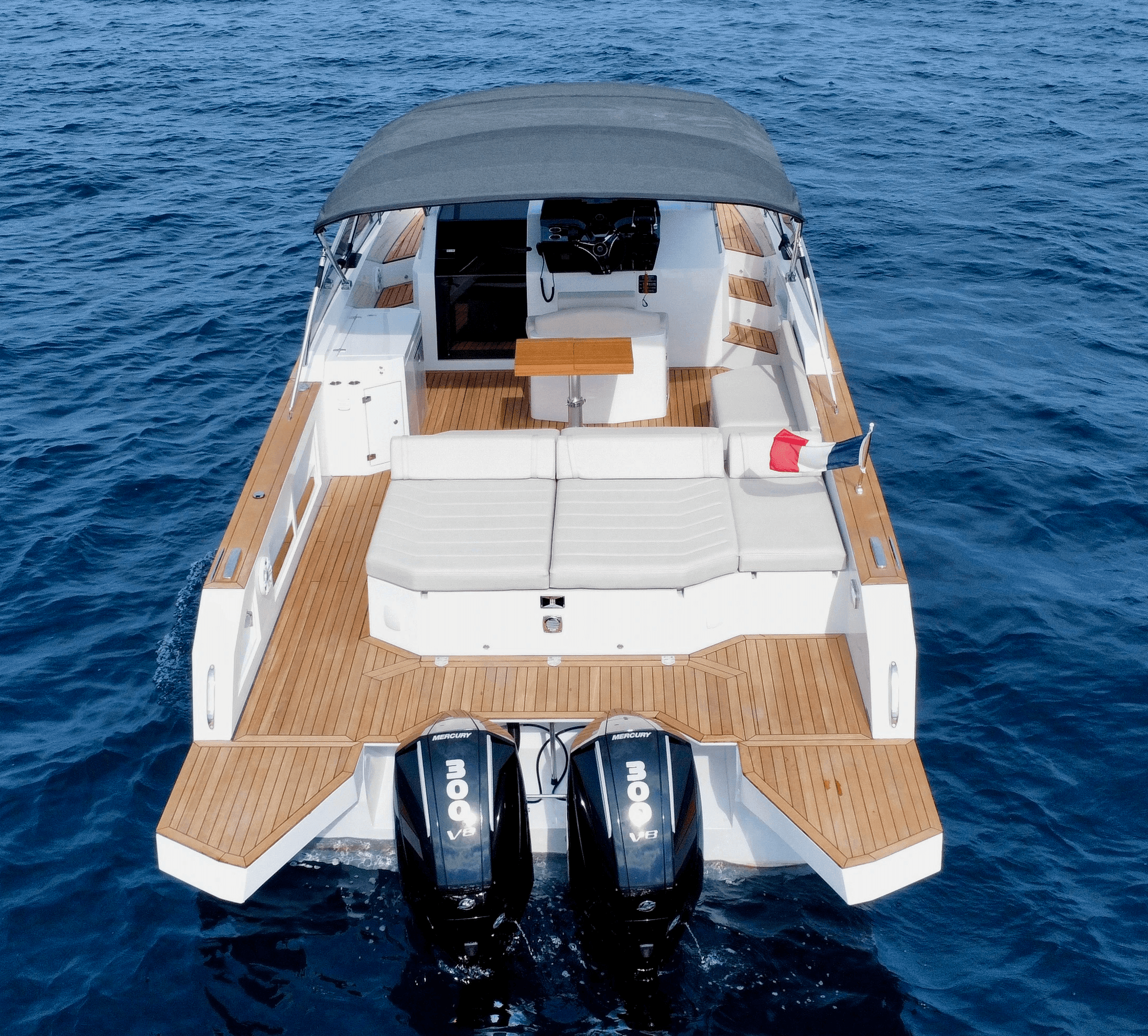 L'image montre un yacht élégant et moderne avec un pont en teck spacieux et deux moteurs hors-bord, naviguant sur une eau bleue vibrante.