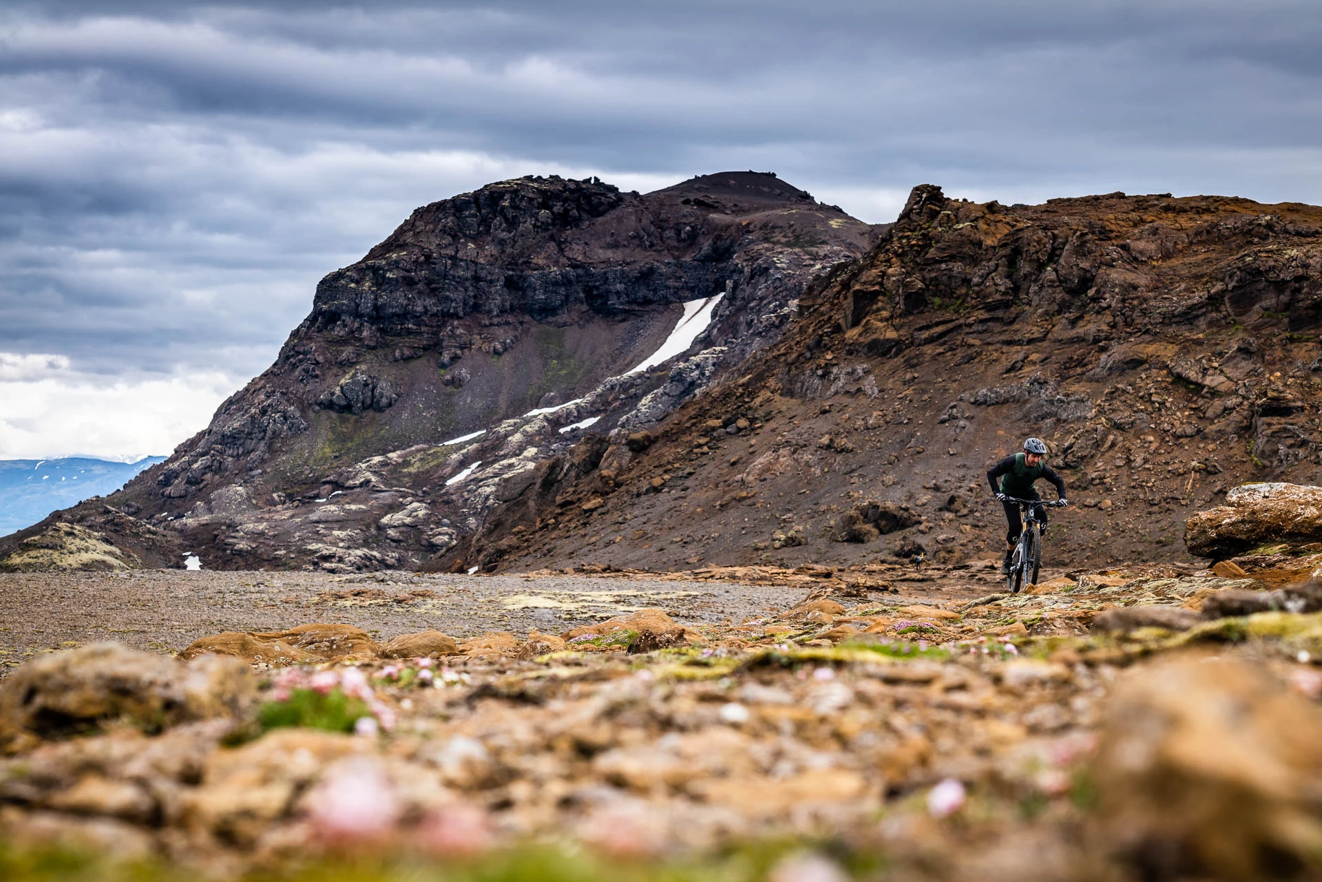 Mountain biker riding across a rocky volcanic plateau beneath overcast skies.