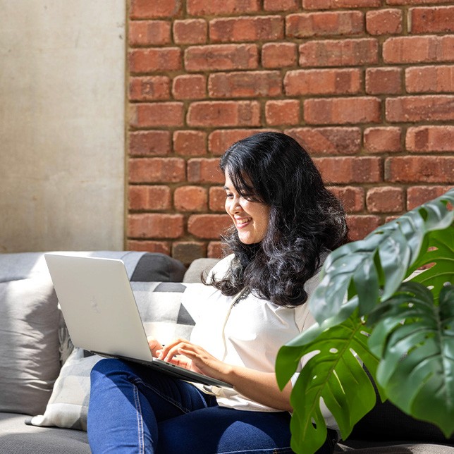 A side profile image of our team member, Pradnya, who is using her laptop while sitting on a sofa.