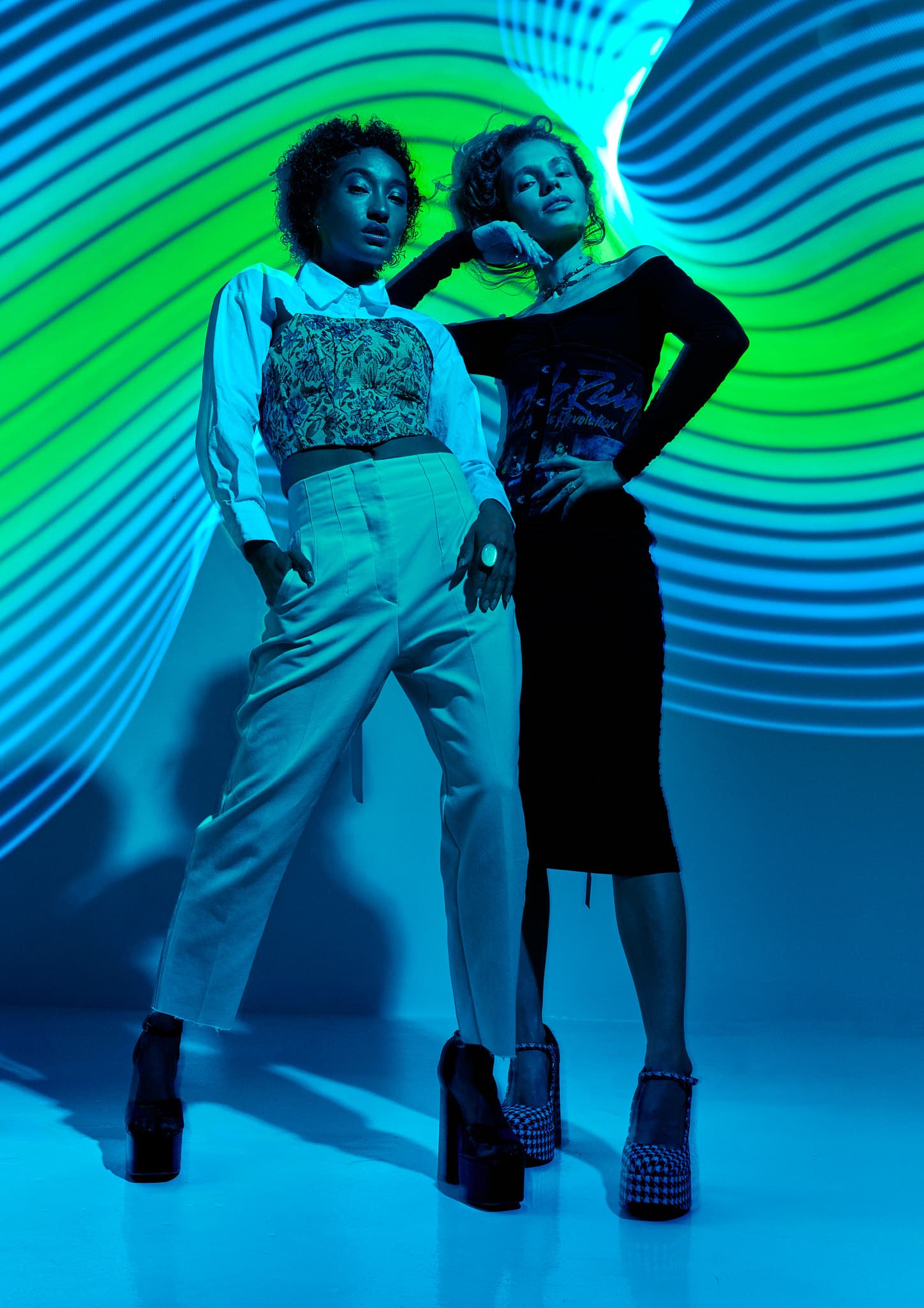 Two models stand under neon blue and green light patterns, showcasing bold fashion at Revelator Studio, a photography studio in Shreveport.