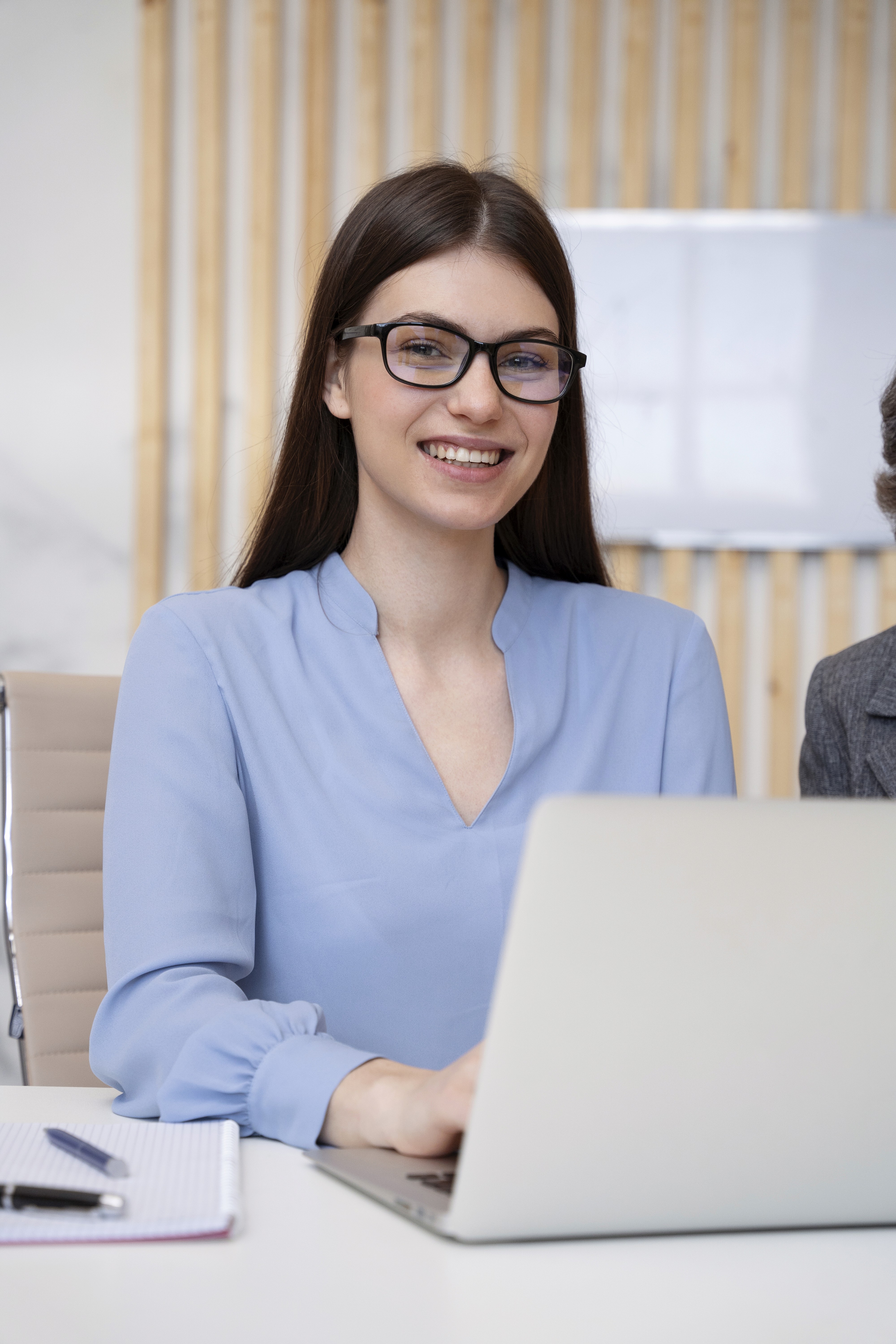 A smiling woman with her arms crossed, standing against a dark green background. She has long, dark hair.