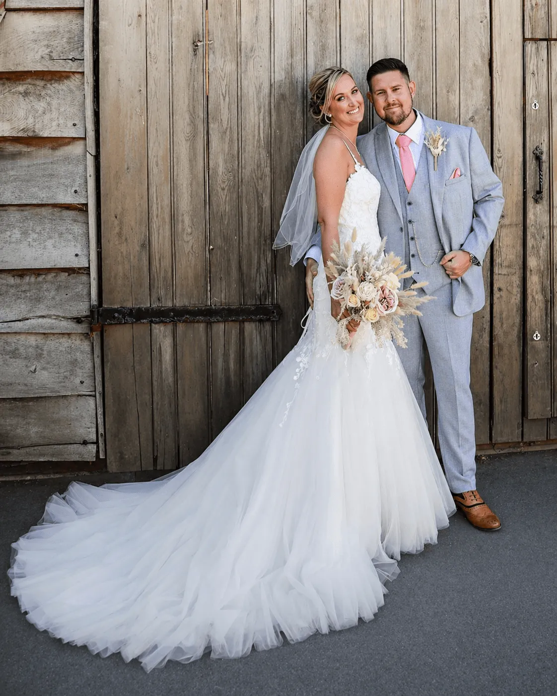 A bride in a white lace wedding dress holds a colorful bouquet of pink, yellow, and orange flowers.