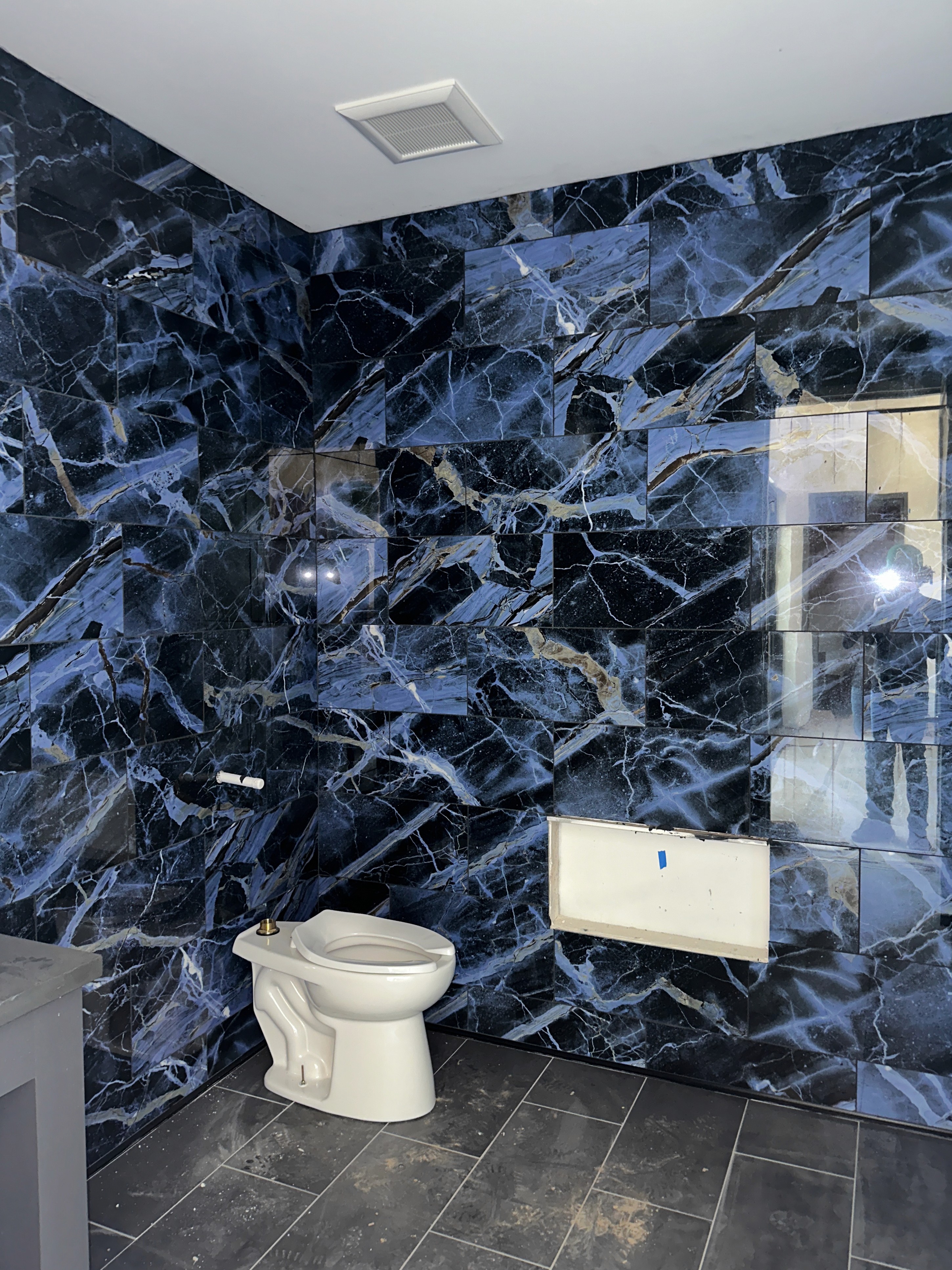 Contemporary bathroom with a blue marble tile wall and a white toilet under recessed lighting.