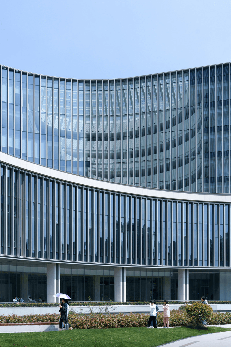 Elegant stone building facade with French balcony windows and a wide entrance framed by glass panels, viewed on a rainy street with reflections on the wet pavement.