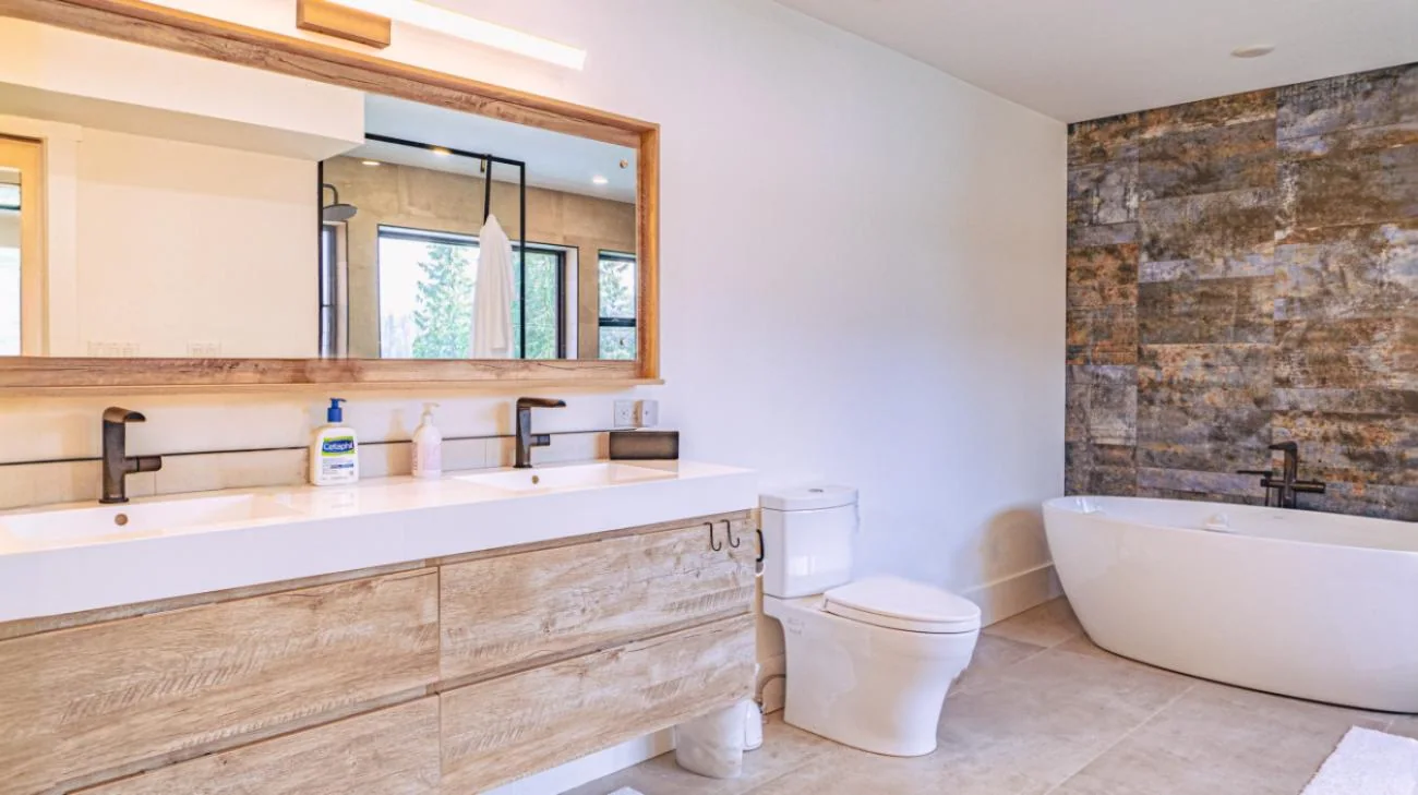 Modern ensuite bathroom featuring dual-sink floating vanity with wood grain finish, vessel sinks, large mirror, and freestanding tub in Vancouver home