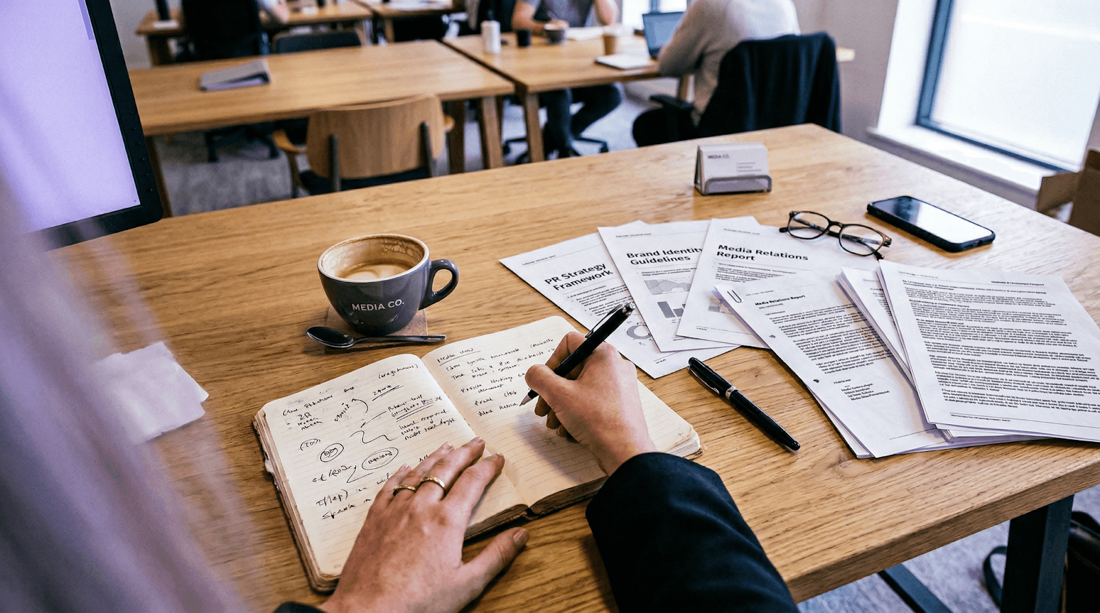 PR communications workspace with notes and printed coverage, representing the manual work behind traditional media monitoring