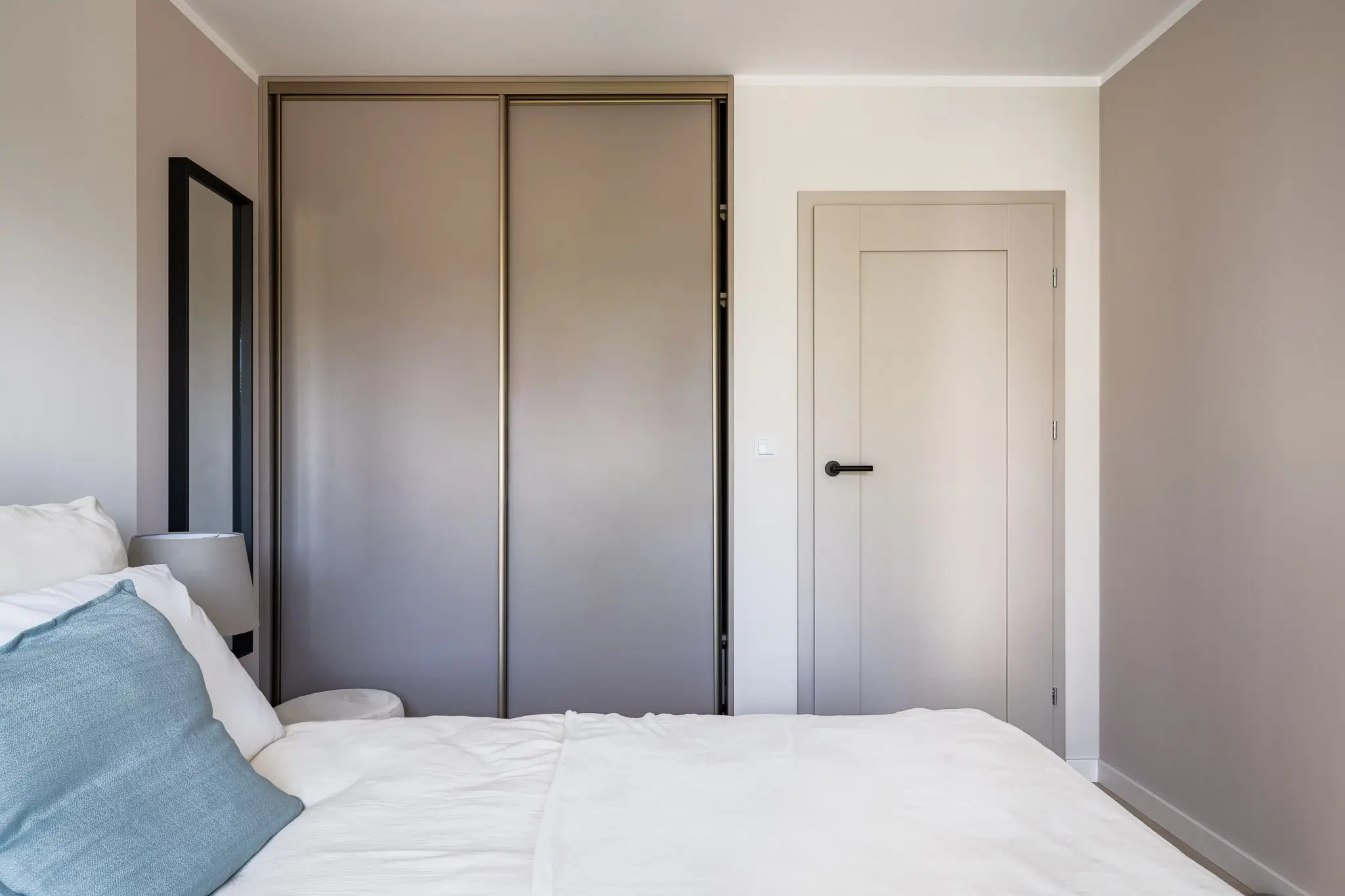 Szafa przesuwna z matowymi frontami w sypialni, dopasowana kolorystycznie do drzwi wewnętrznych.