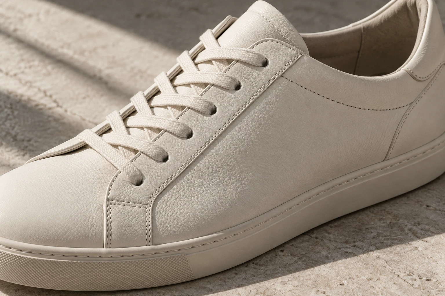 Conceptual close view of ivory sneaker laces, stitching and rubber sidewall on pale stone