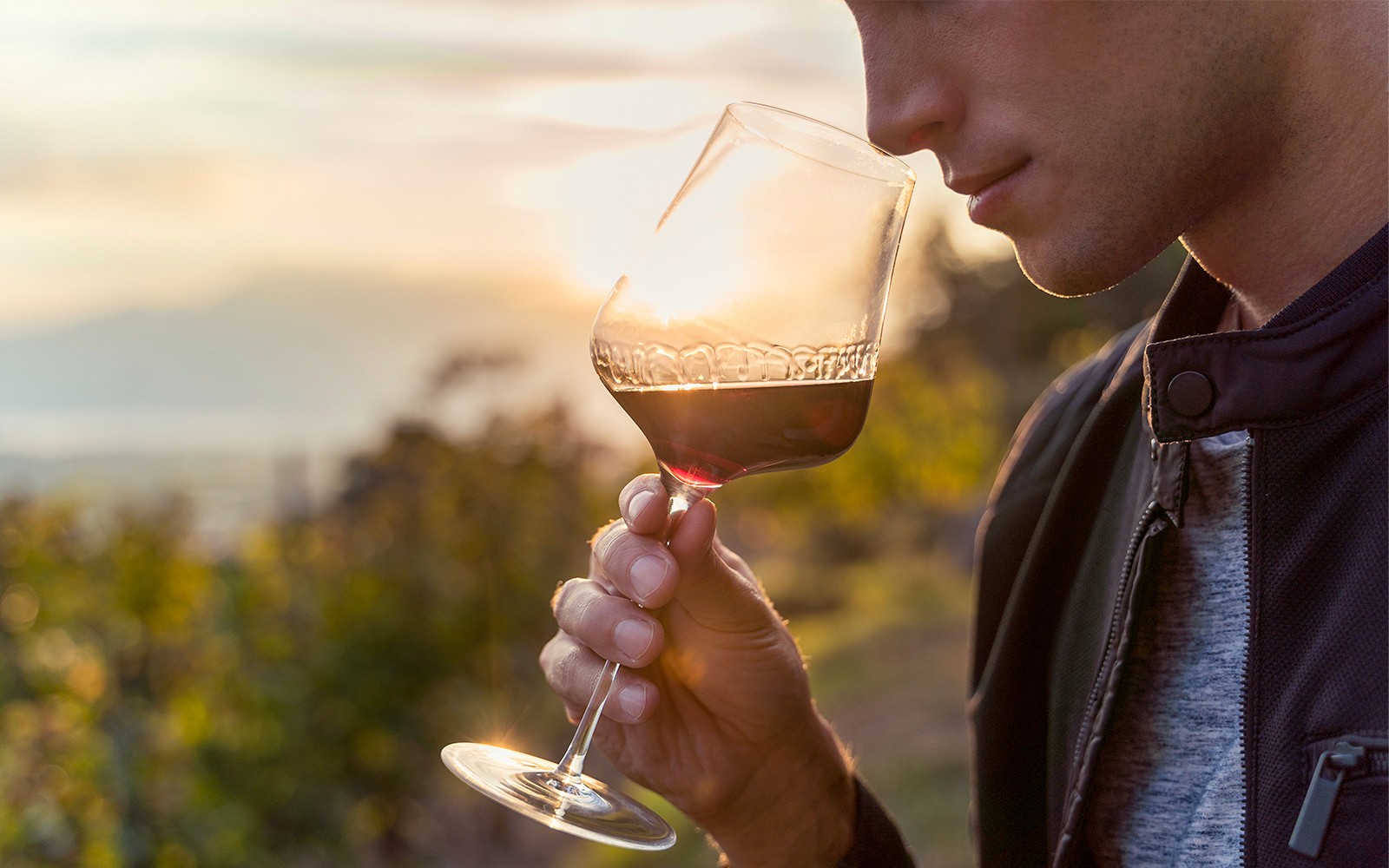 Man savoring wine outdoors at sunset.